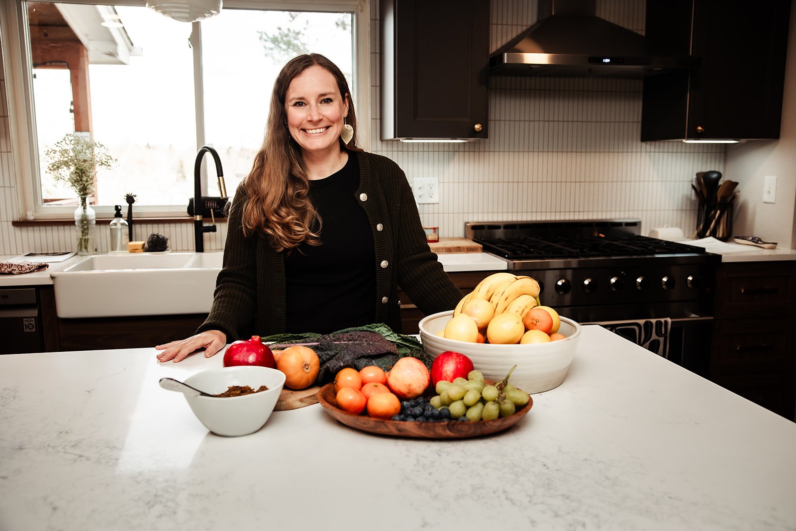 Karina Wenker, Nutritionist, smiling, standing in the kitchen with nourishing food laid out in front of her