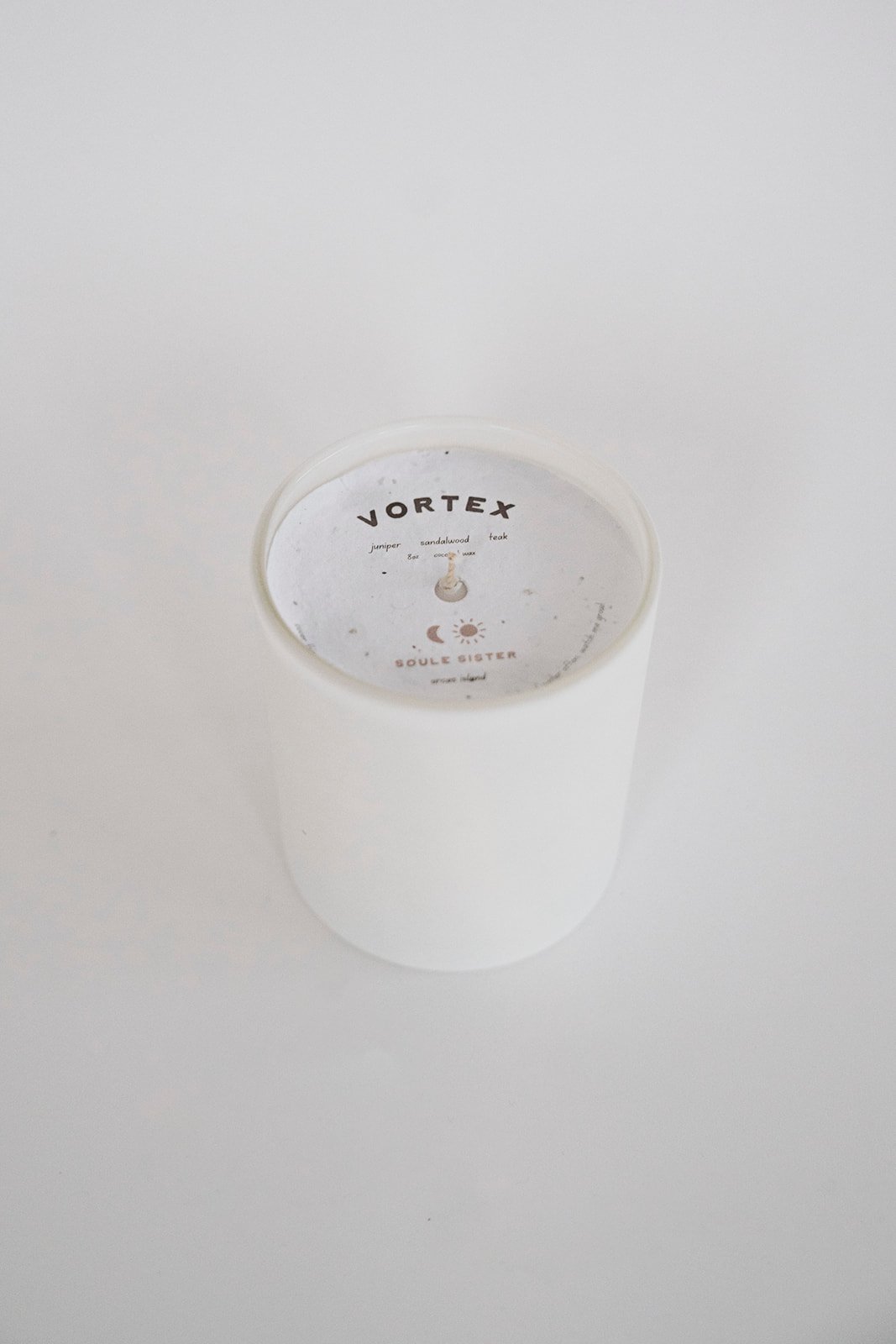 A white cylindrical container with a round transparent lid, labeled 'VORTEX' with notes about scent notes and a moon and sun graphic.