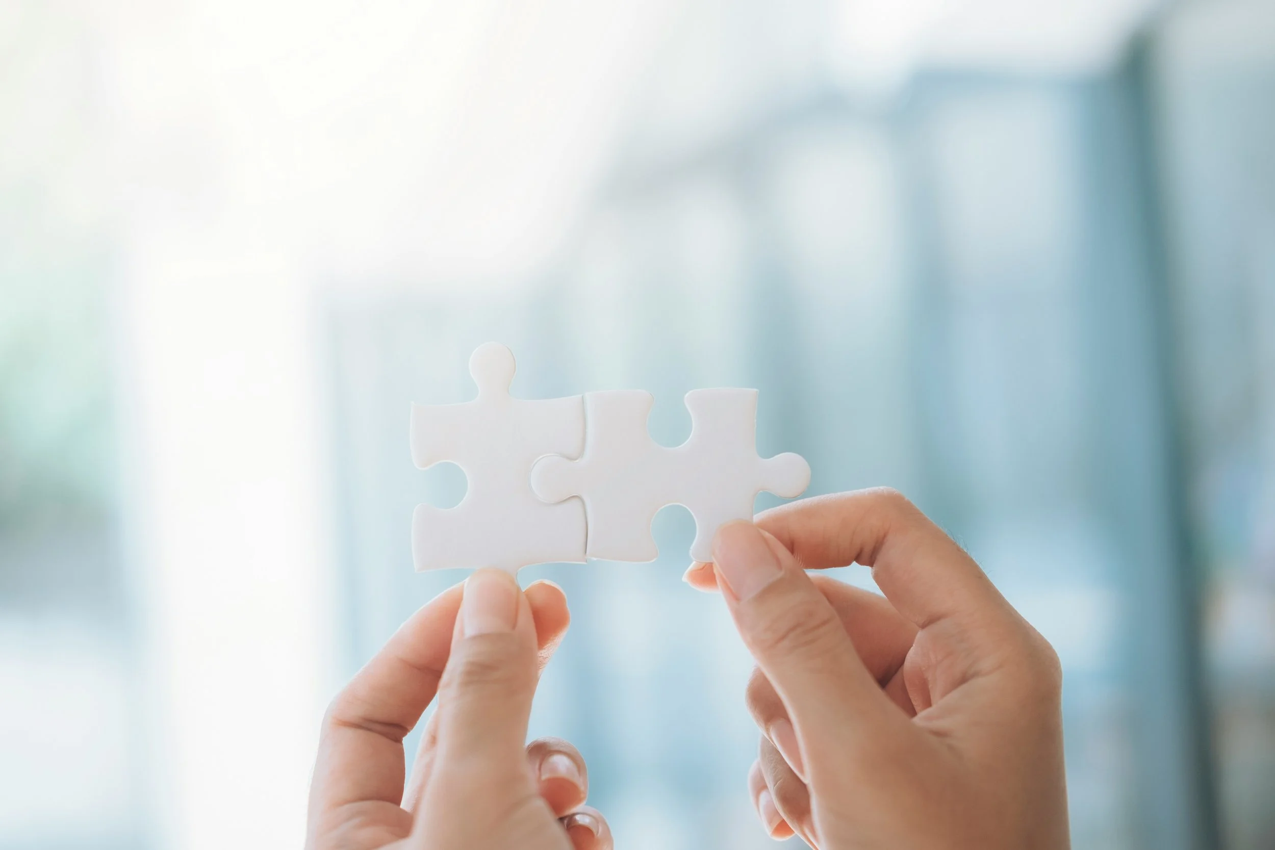 woman's hands holding up two connecting white puzzle pieces against a blurry blue background
