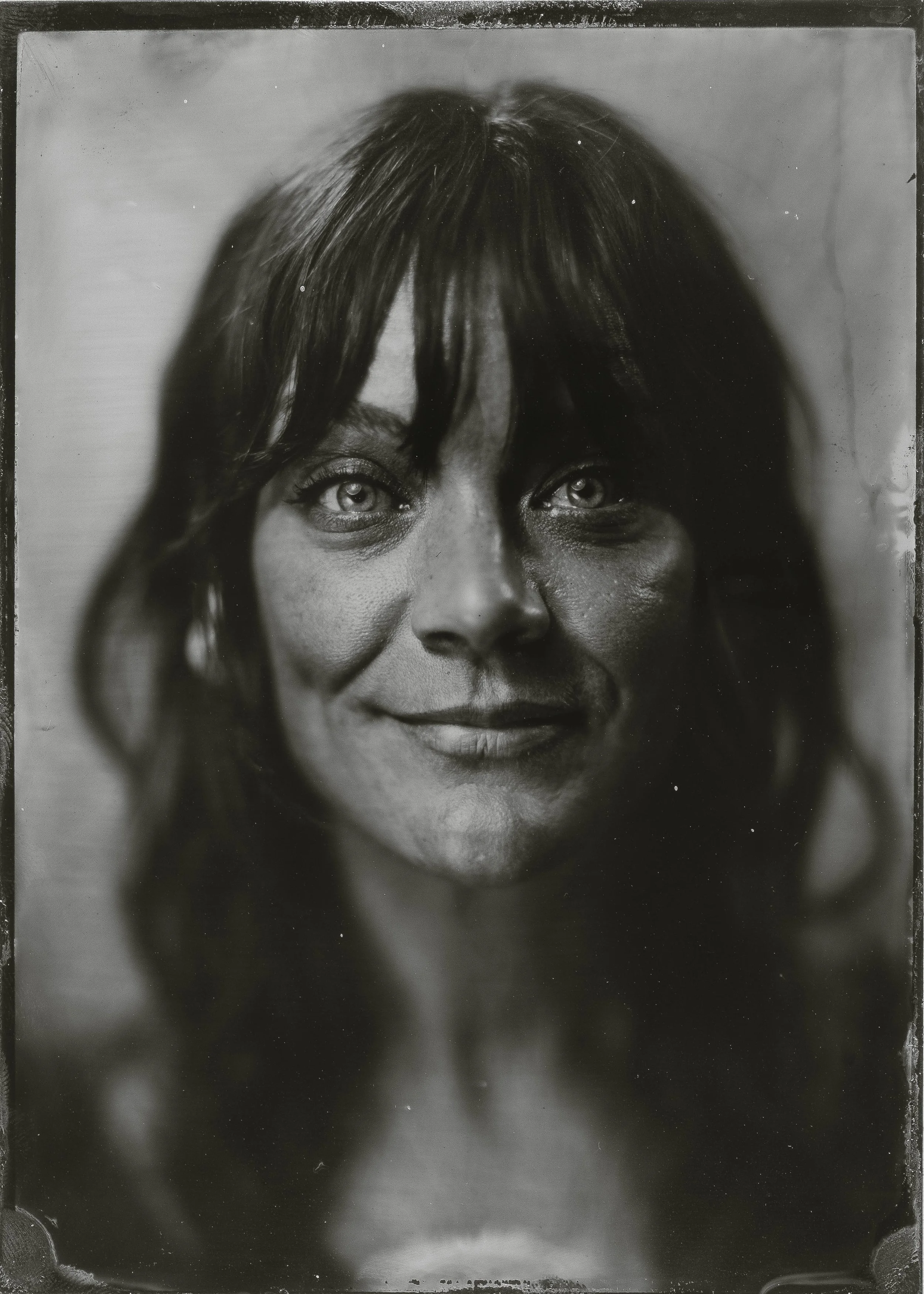 Black-and-white portrait photograph of a woman with shoulder-length hair and light eyes, smiling softly.