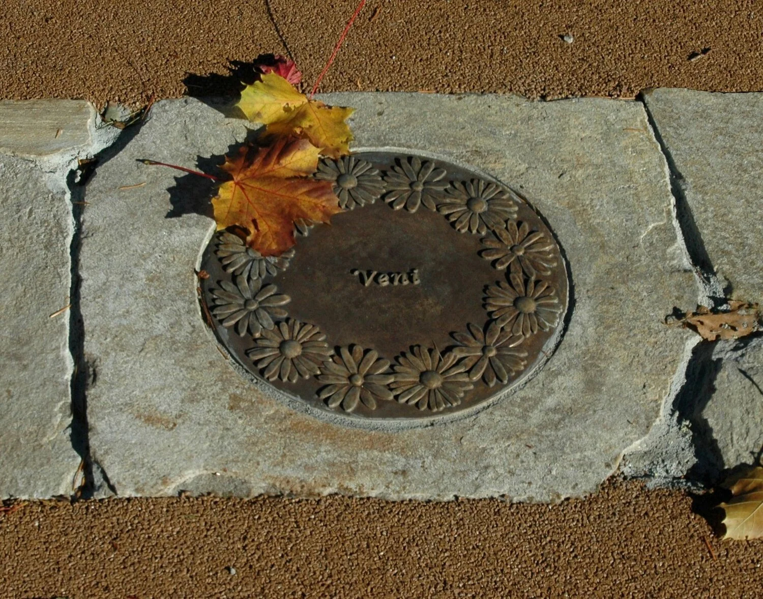 A bronze medallion placed within the first stepping stone adorned with the crown of daisy welcomes one with the beginning verse of the Carmelite profession “Veni,” “Come.”