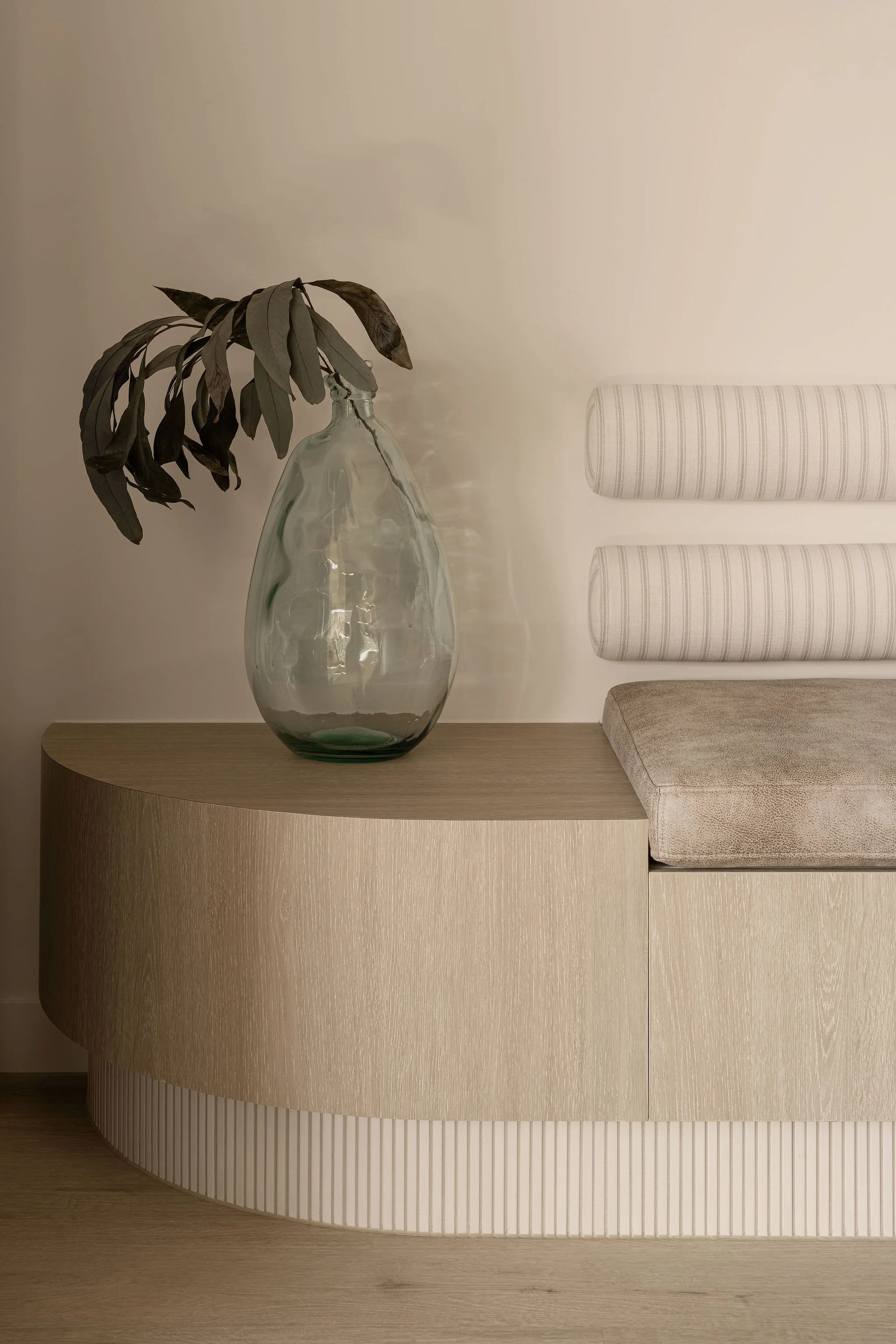 Sunshine Retreat, curved oak joinery bench with fluted base, glass vase and striped bolster cushions