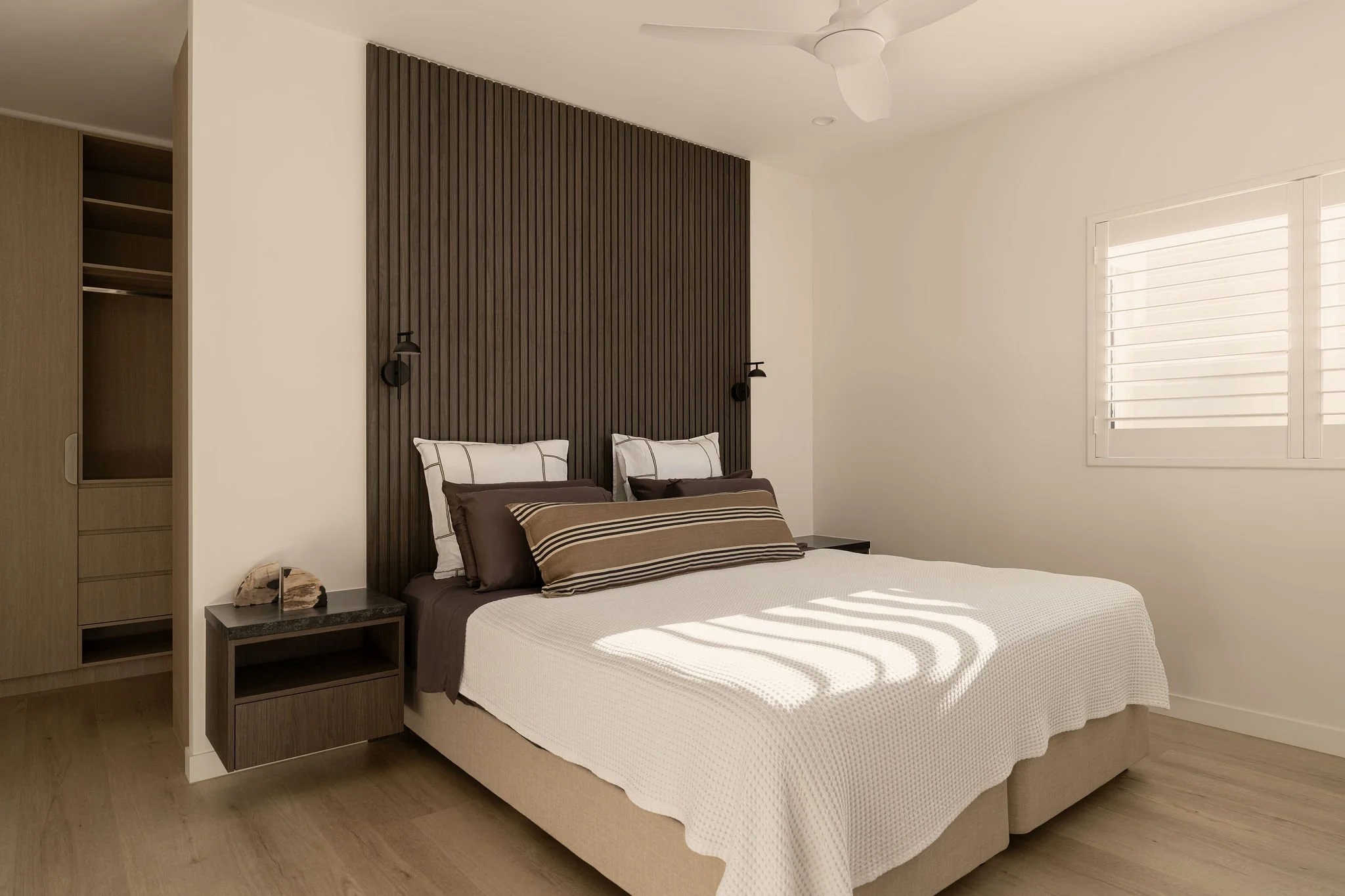 Sunshine Retreat, renovated bedroom with dark slatted timber feature wall, black wall lights and striped cushions