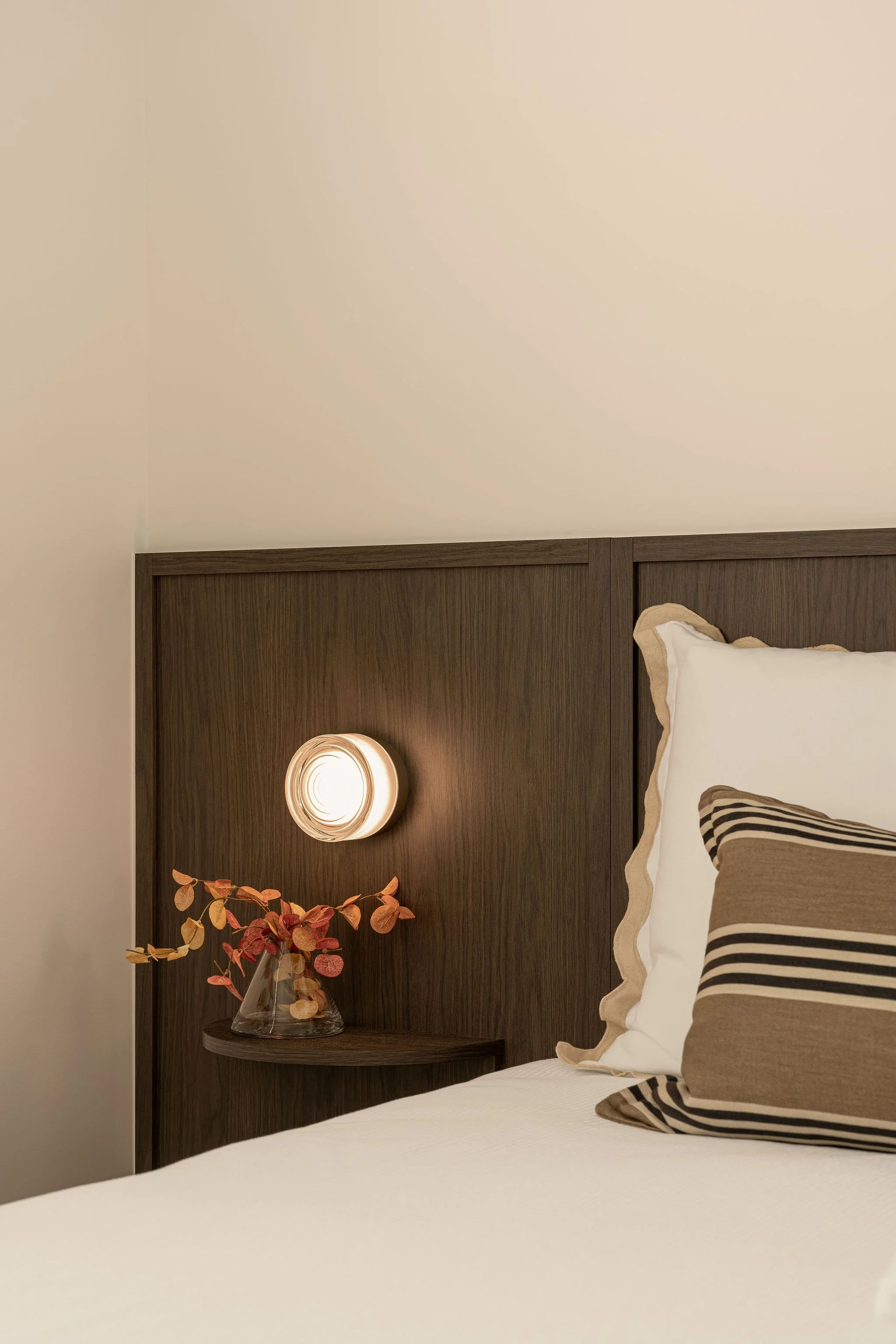 Sunshine Retreat, bedside detail of a dark timber bedhead with round wall light, dried flowers and striped cushions