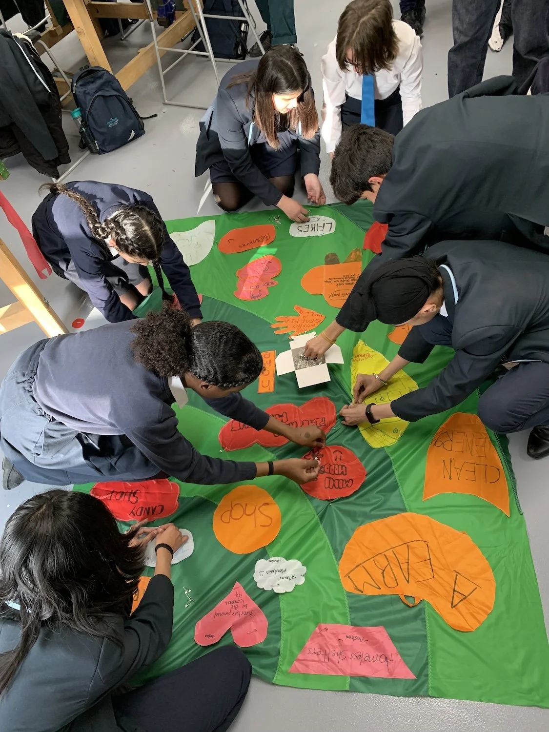 Students working together on a project about climate change, creating a large colorful poster with words and shapes related to climate and environmental issues.