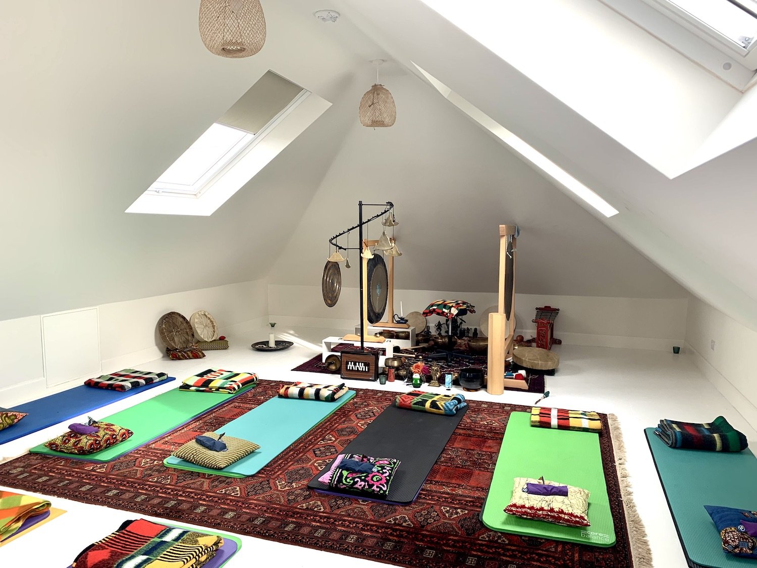 A meditation room with yoga mats, cushions, and traditional musical instruments on a Persian rug under a sloped ceiling with skylights.