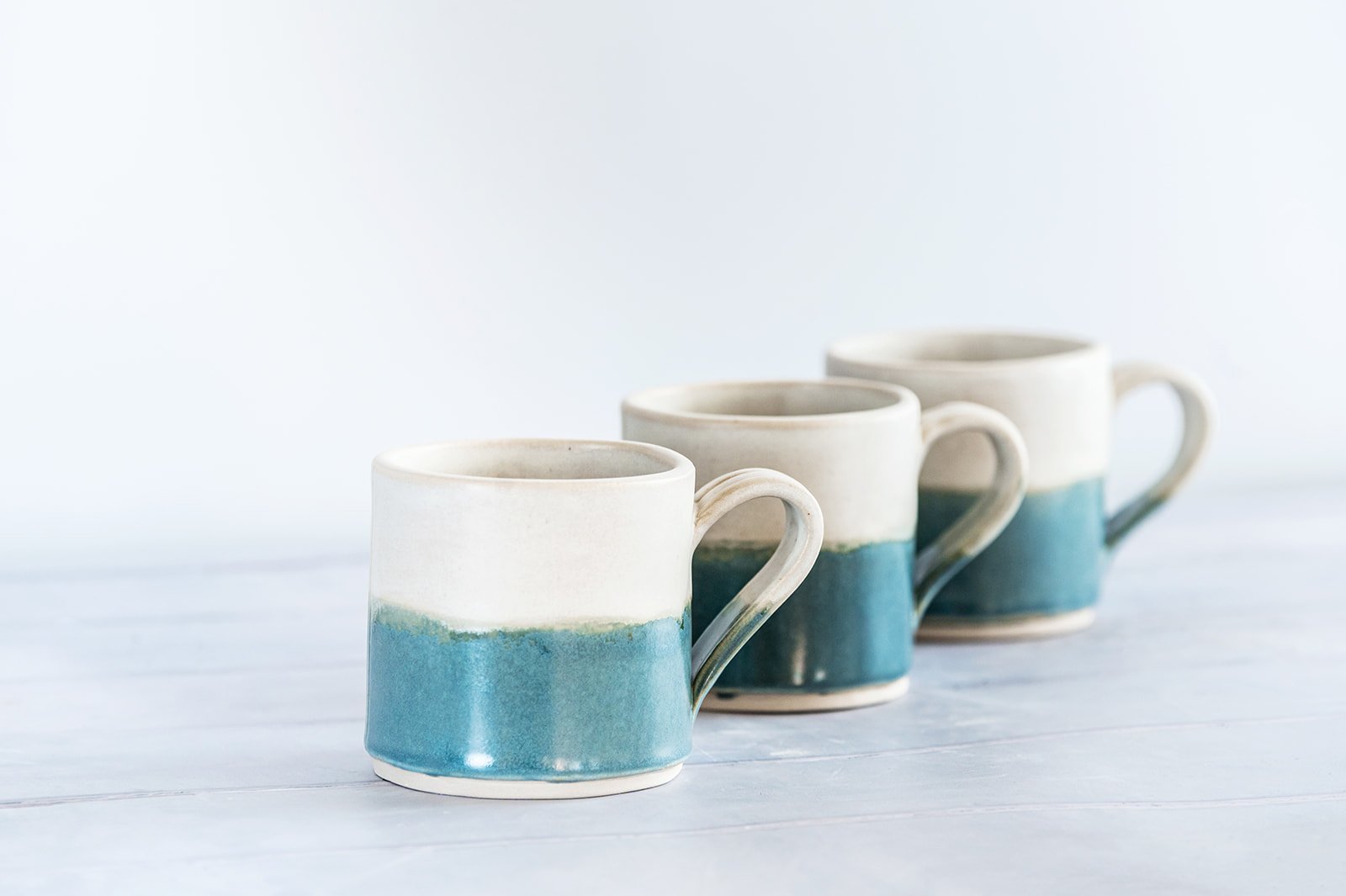 Three handmade stoneware mugs in sea blue and American alabaster glaze, made by Isil Ceramics in the New Forest.