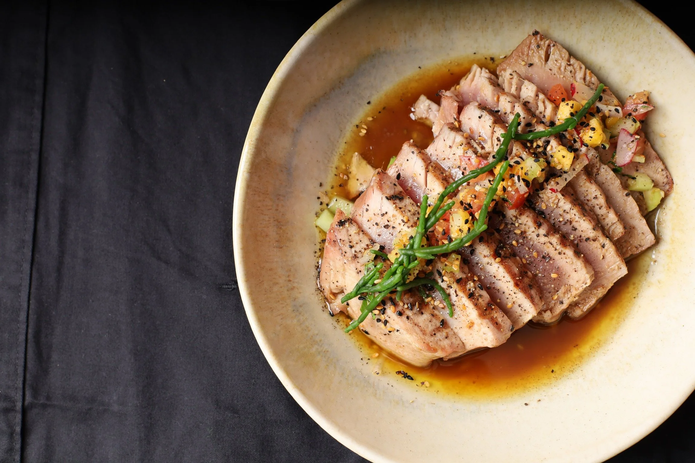 Gekookte tonijn met sesamzaad, geserveerd met een saus en fijngesneden groenten, gegarneerd met lente-ui op een bord