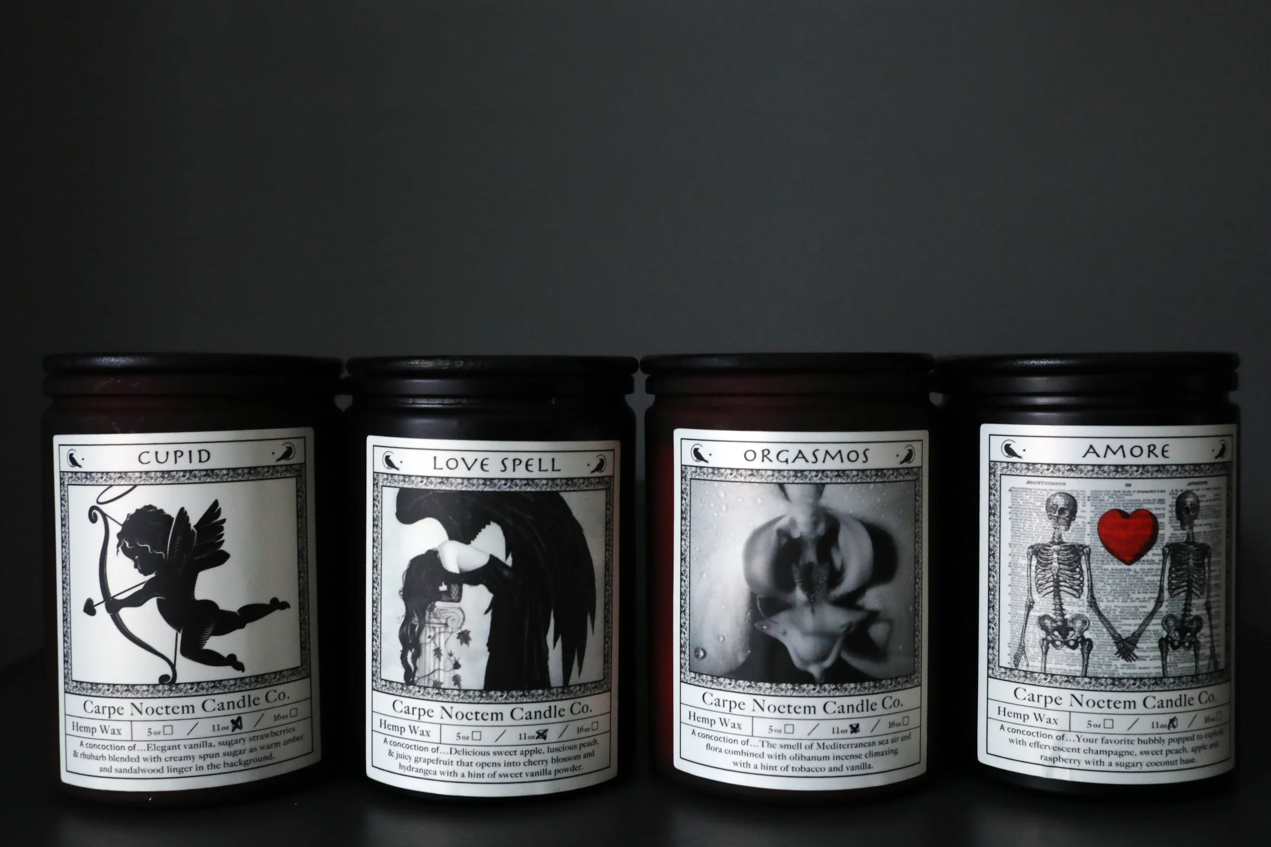 Four candles with labels 'Cupid,' 'Love Spell,' 'Orgasmos,' and 'Amore,' each with different black and white label designs, placed side by side.