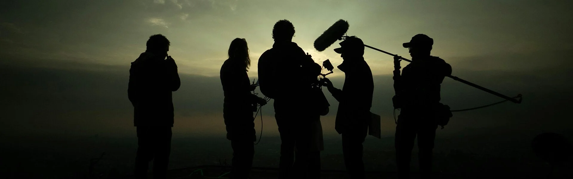 Small video crew silhouetted during filming, showing how camera operation relies on coordination across a lean production team