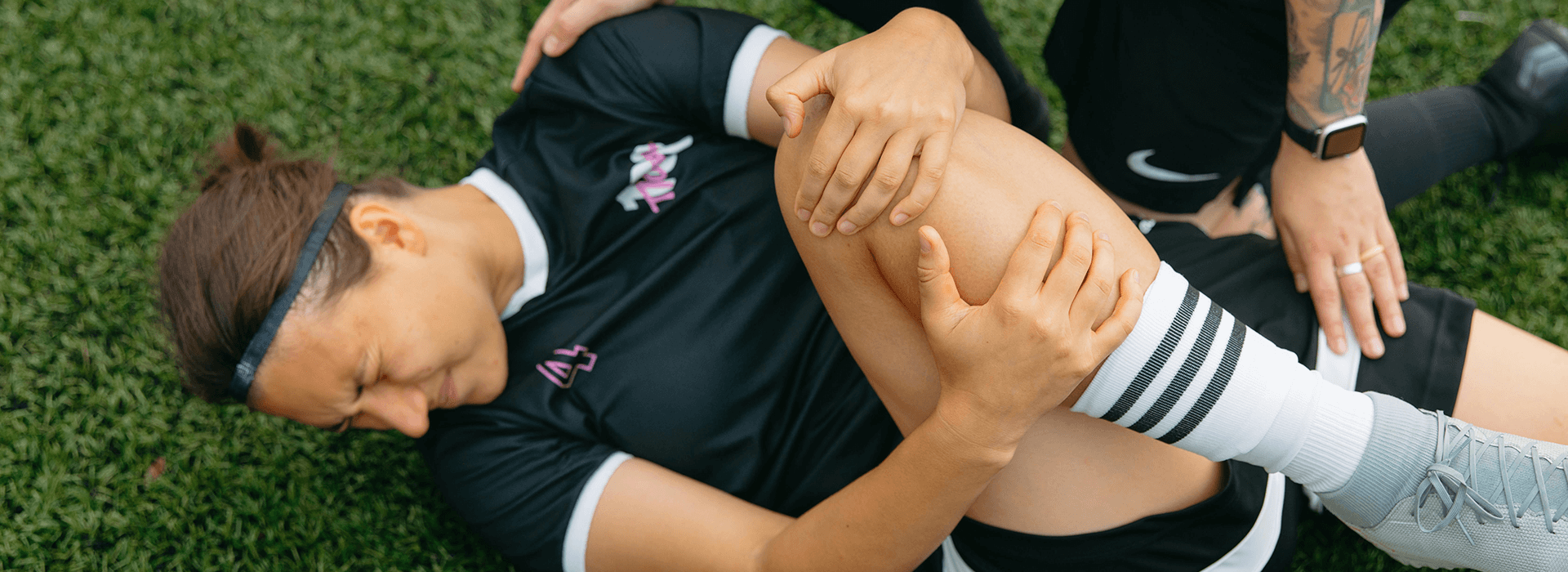 Football player on the grass holding her injured leg during training before an important match