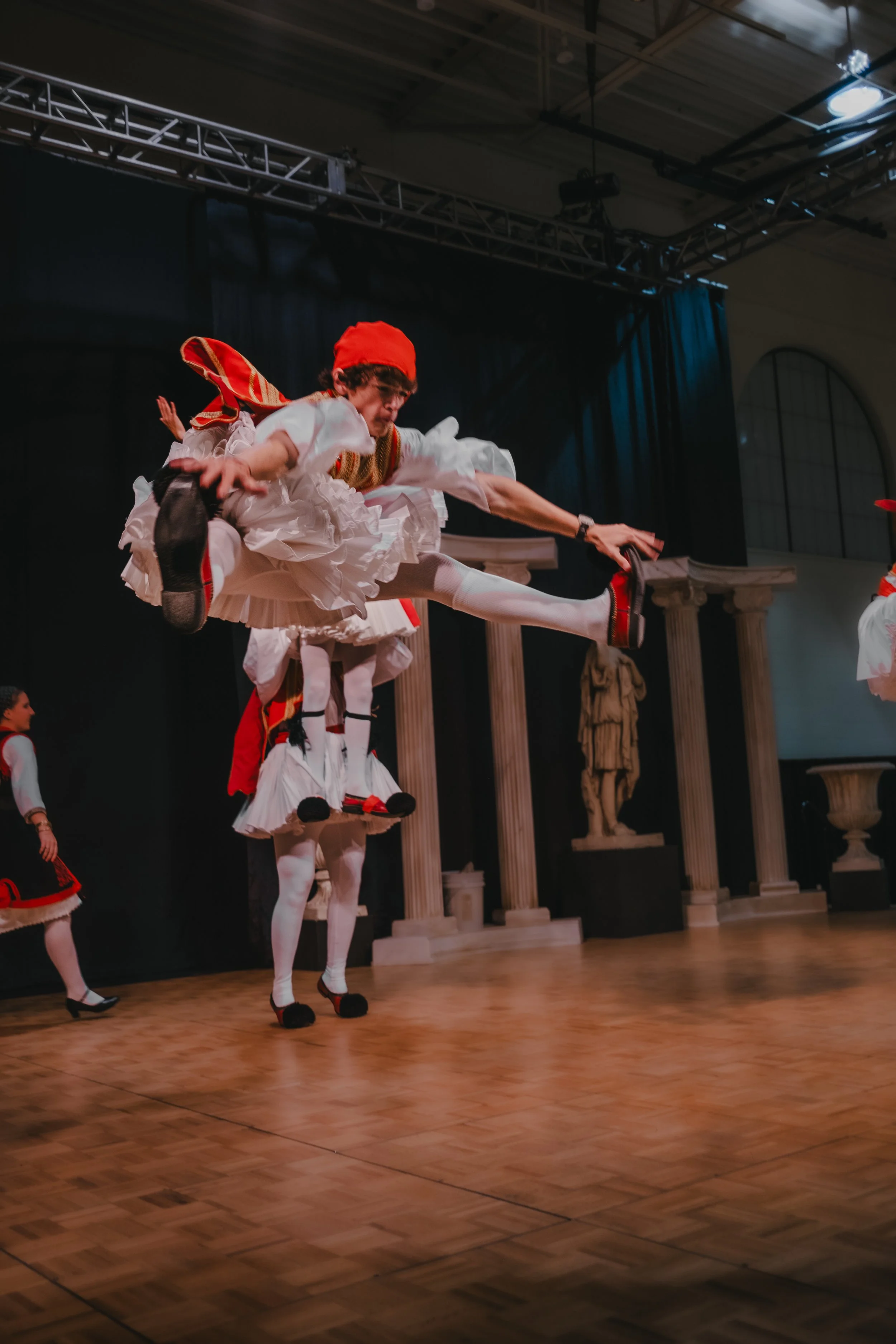 A dancer in traditional folk costume performing a high jump during a stage dance performance.