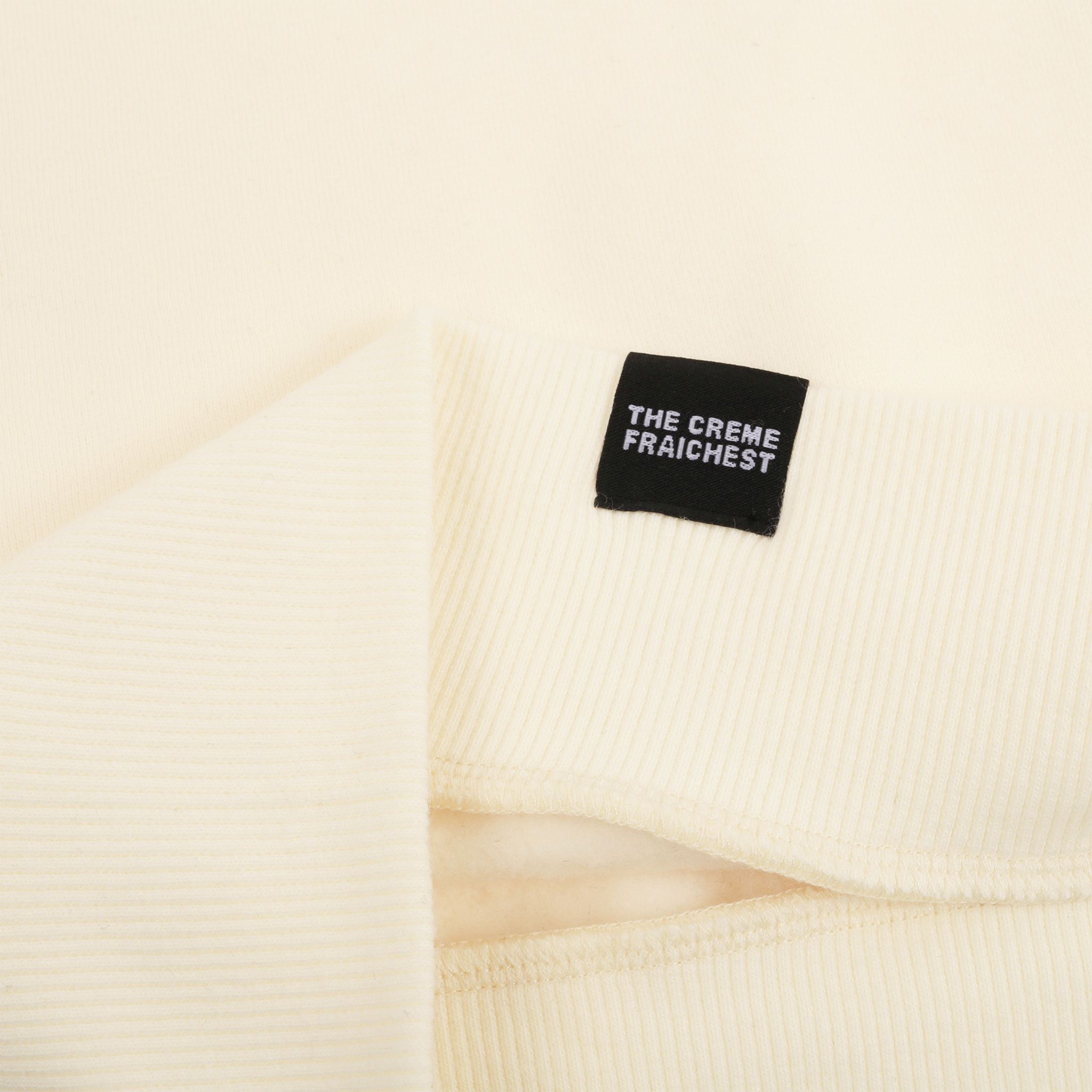 Close-up of a cream-colored garment with a black label that reads 'THE CREME FRAICH'