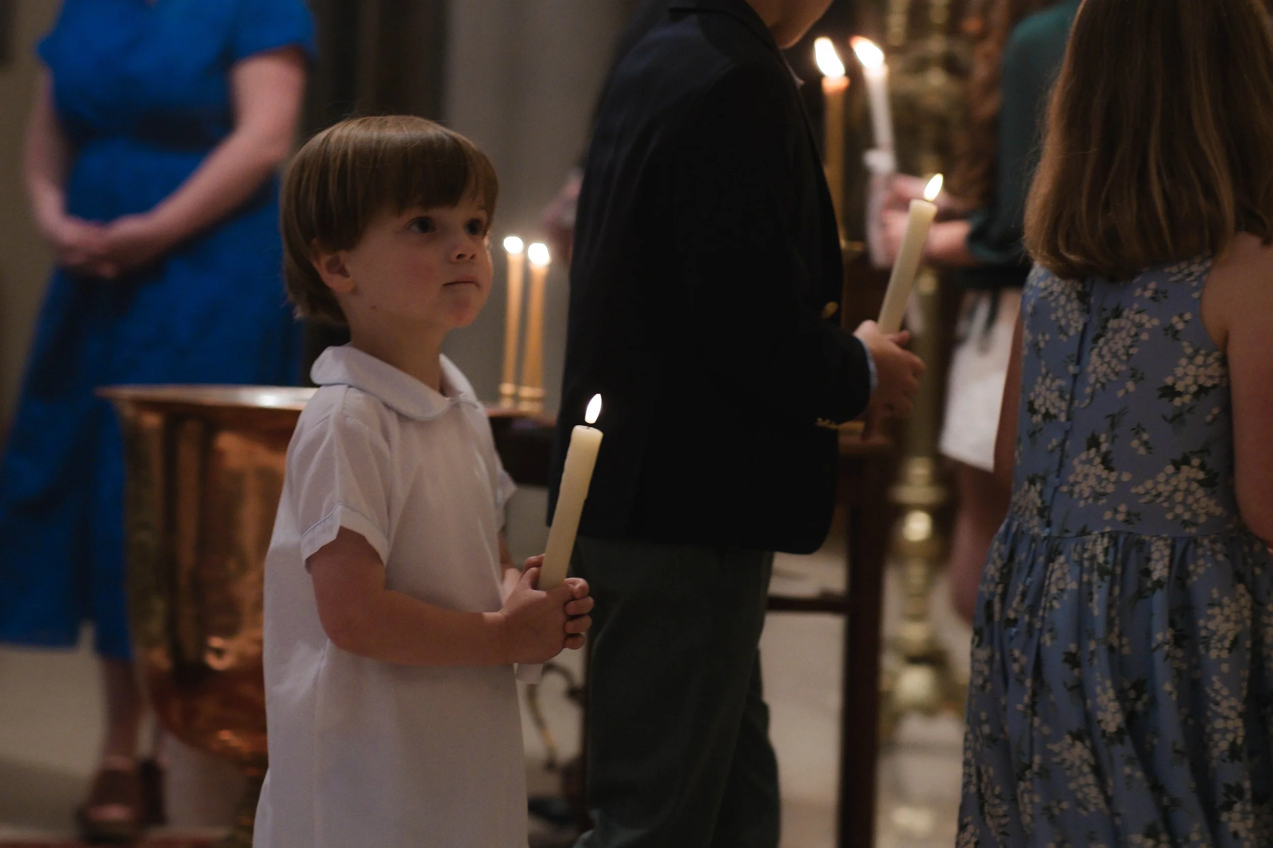 Young boy in a white shirt holding a lit candle during a religious ceremony inside a church.