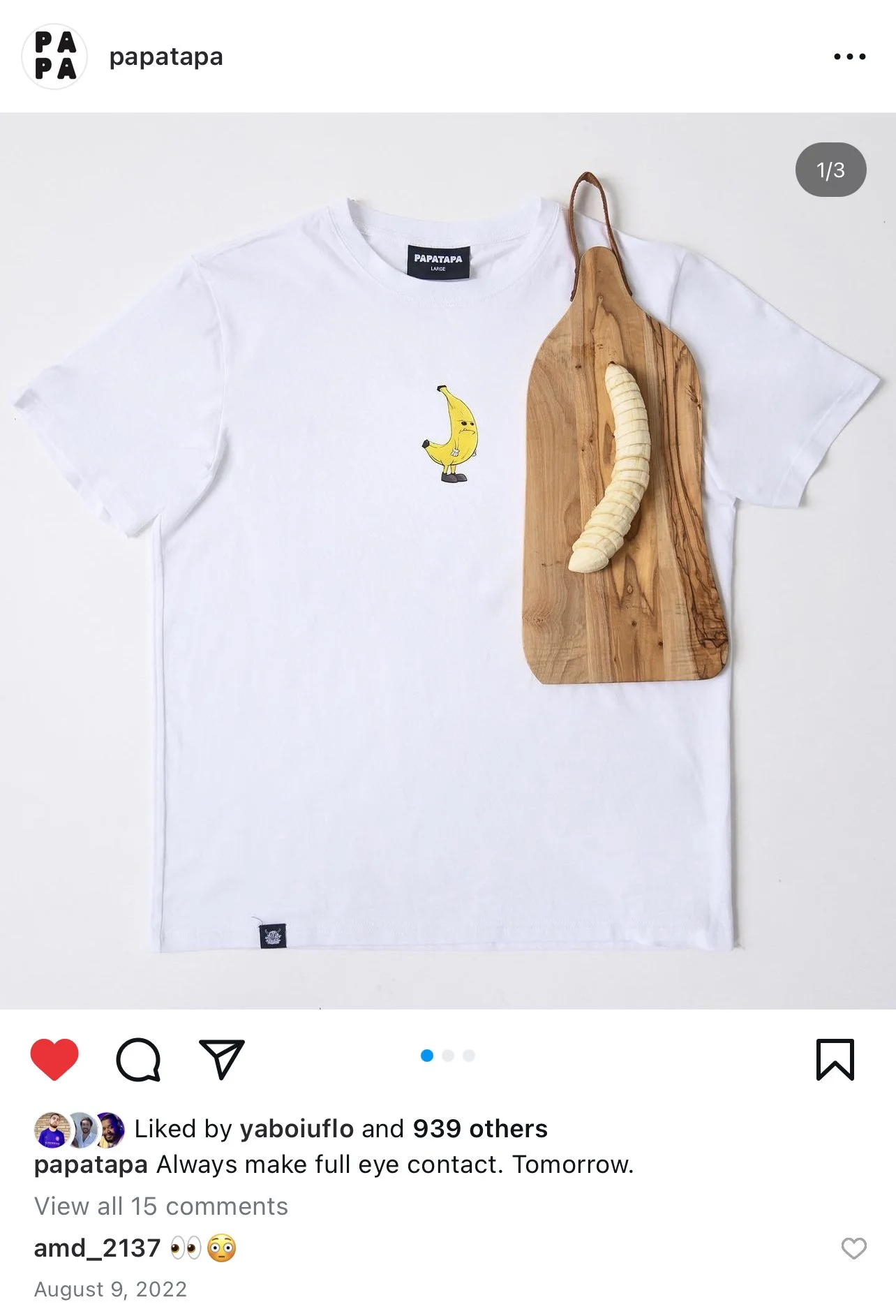 A white T-shirt with a small banana character graphic on it. The T-shirt is placed on a flat surface with a wooden cutting board partially on it. A peeled banana is also on the cutting board, creating a visual resemblance to the banana character on the T-shirt.