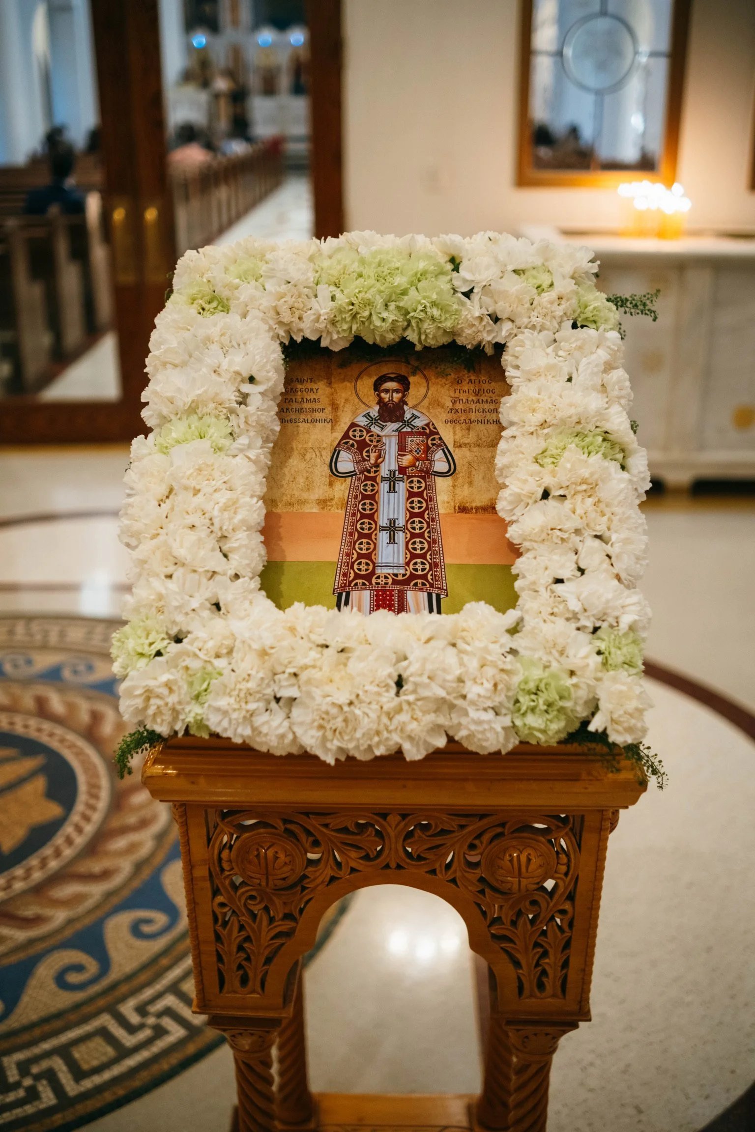 Icon of a saint framed with white flowers on a carved wooden stand inside a church.