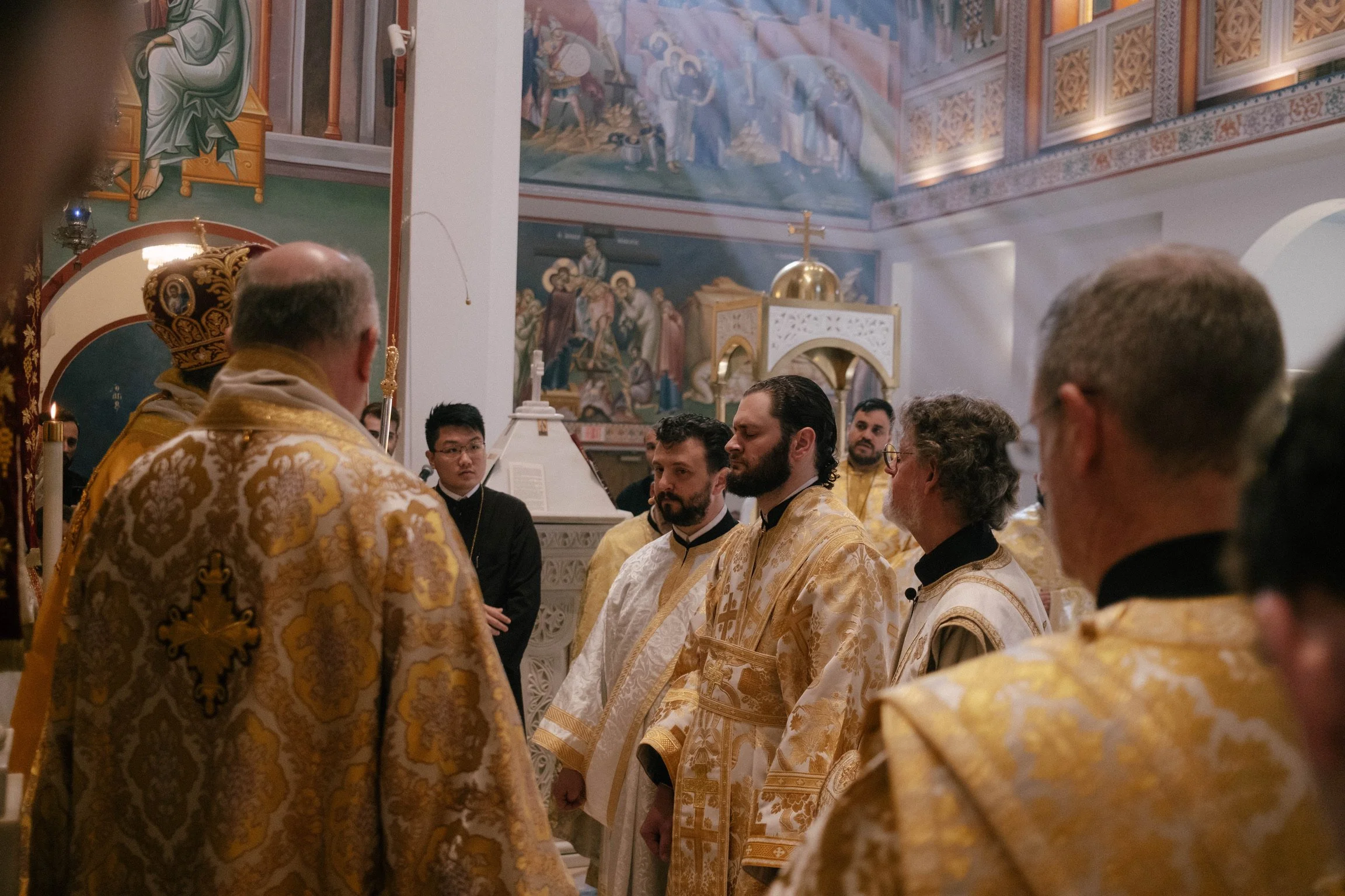 Clergy and altar servers during a religious ceremony inside an ornately decorated church with Christian icons, frescoes, and a gold-domed altar.