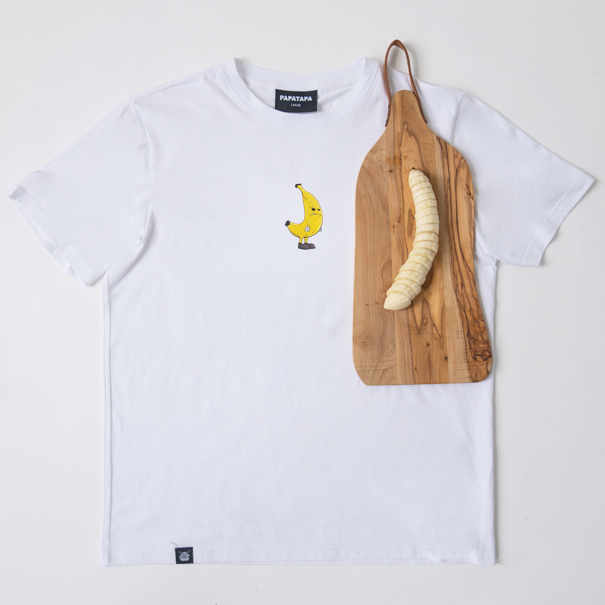 White T-shirt with a banana cartoon graphic and a wooden cutting board with a peeled banana on it.