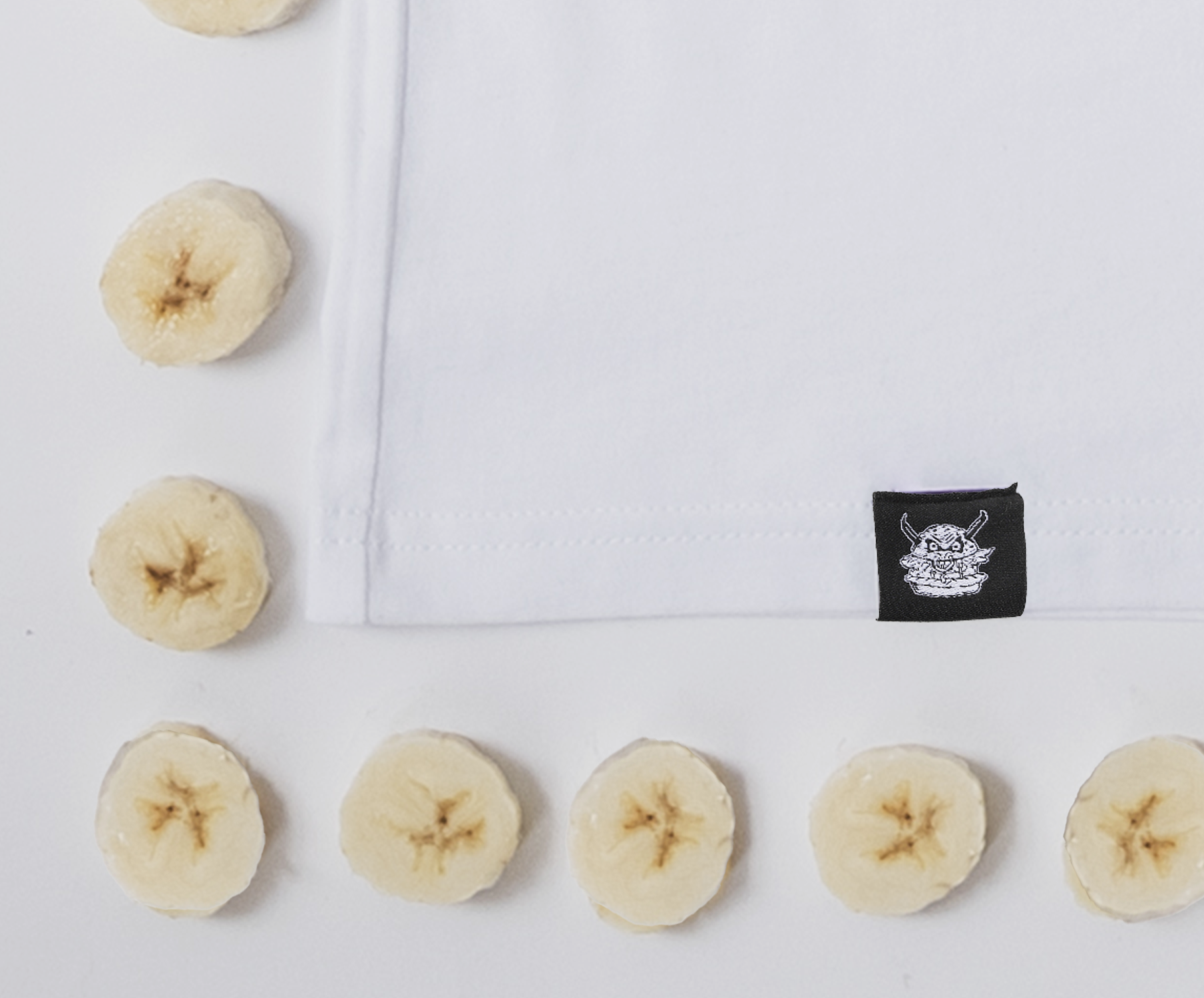 Slices of banana arranged in a U-shape on a white surface with a white cloth in the middle and a black tag featuring a cartoon monster logo.