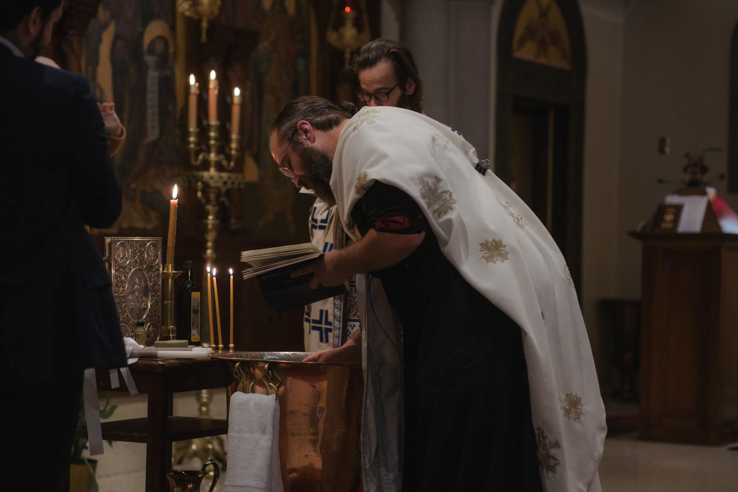Clergy members performing a religious ceremony in a church, with candles and religious icons in the background.