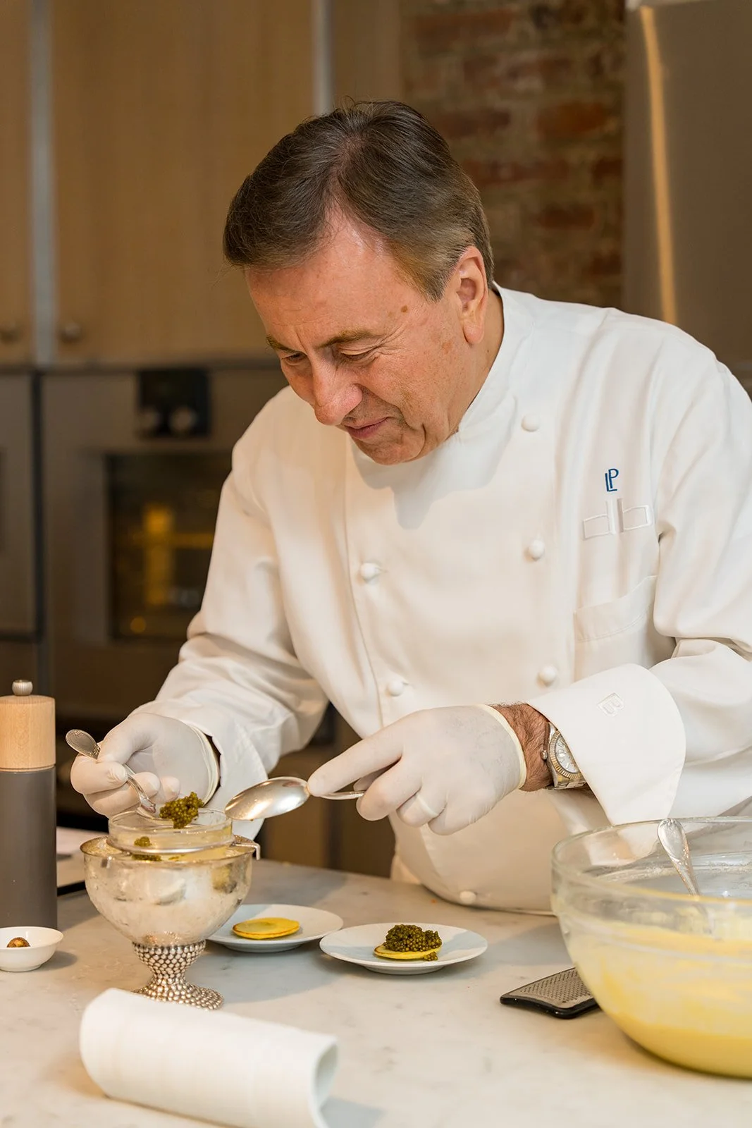 A chef in a white uniform and gloves carefully plates a dish in a kitchen.