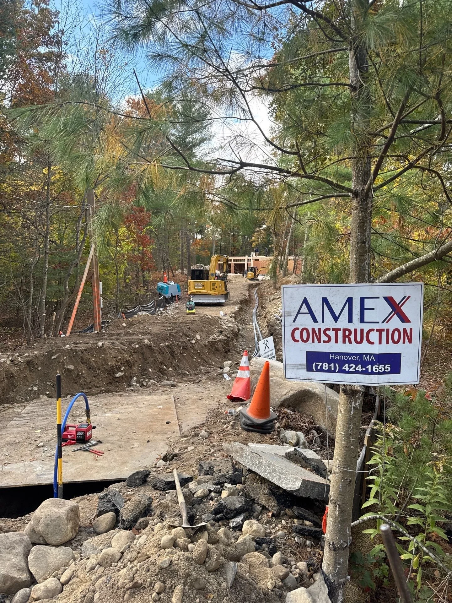 Construction site with heavy machinery, orange cones, and a sign for AMEX Construction in Hanover, MA.