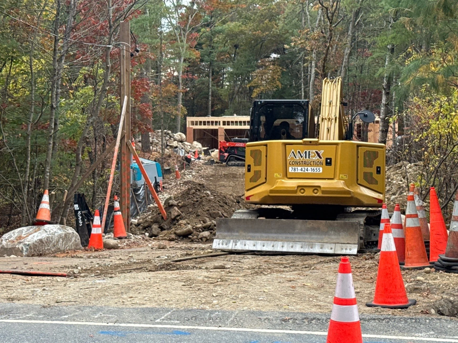 Construction equipment working on a roadway surrounded by orange cones and a wooded area.