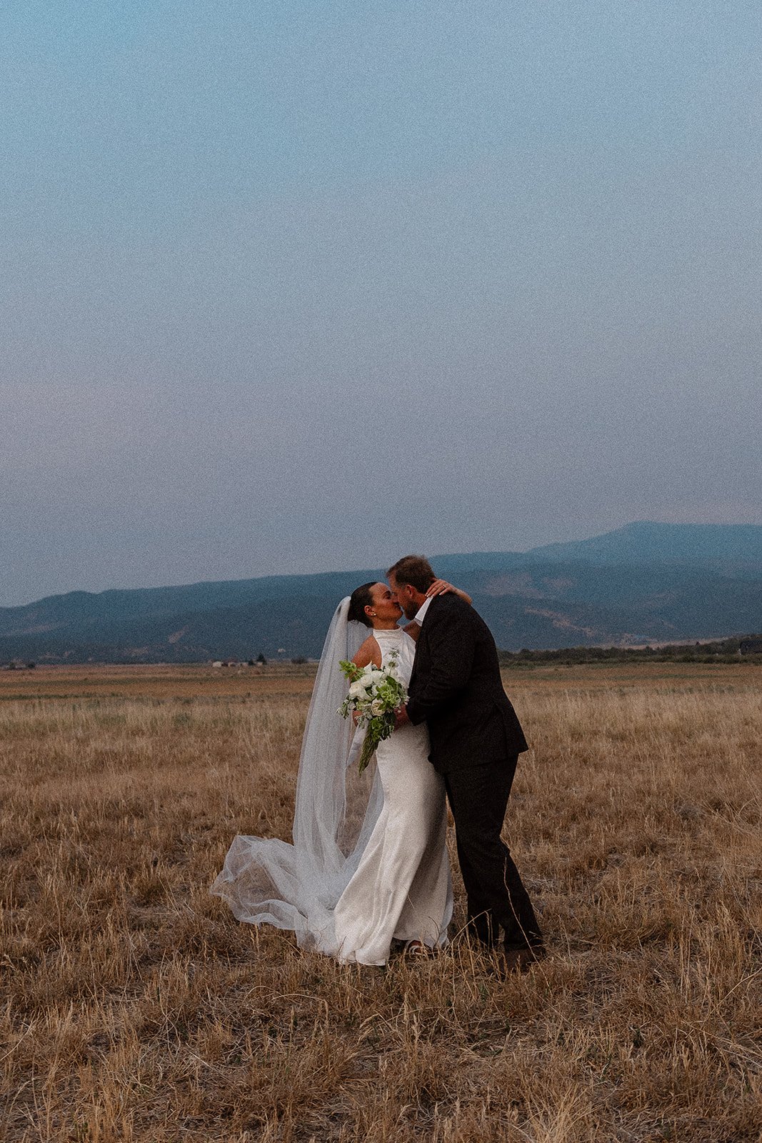 A bride and groom sharing a kiss during their wedding, surrounded by flowers.