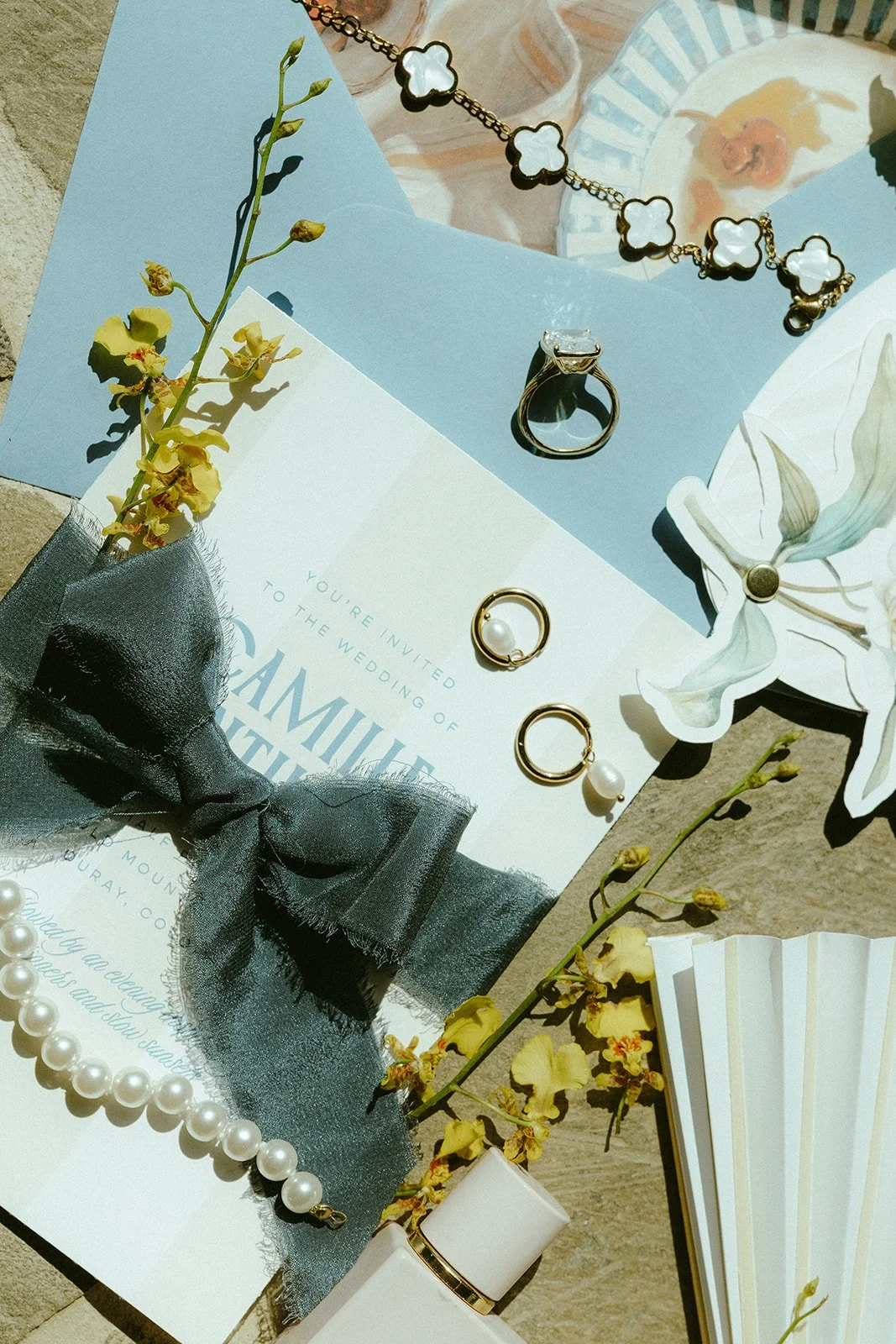 Wedding invitation card with jewelry, flowers, and decorative items on a table.