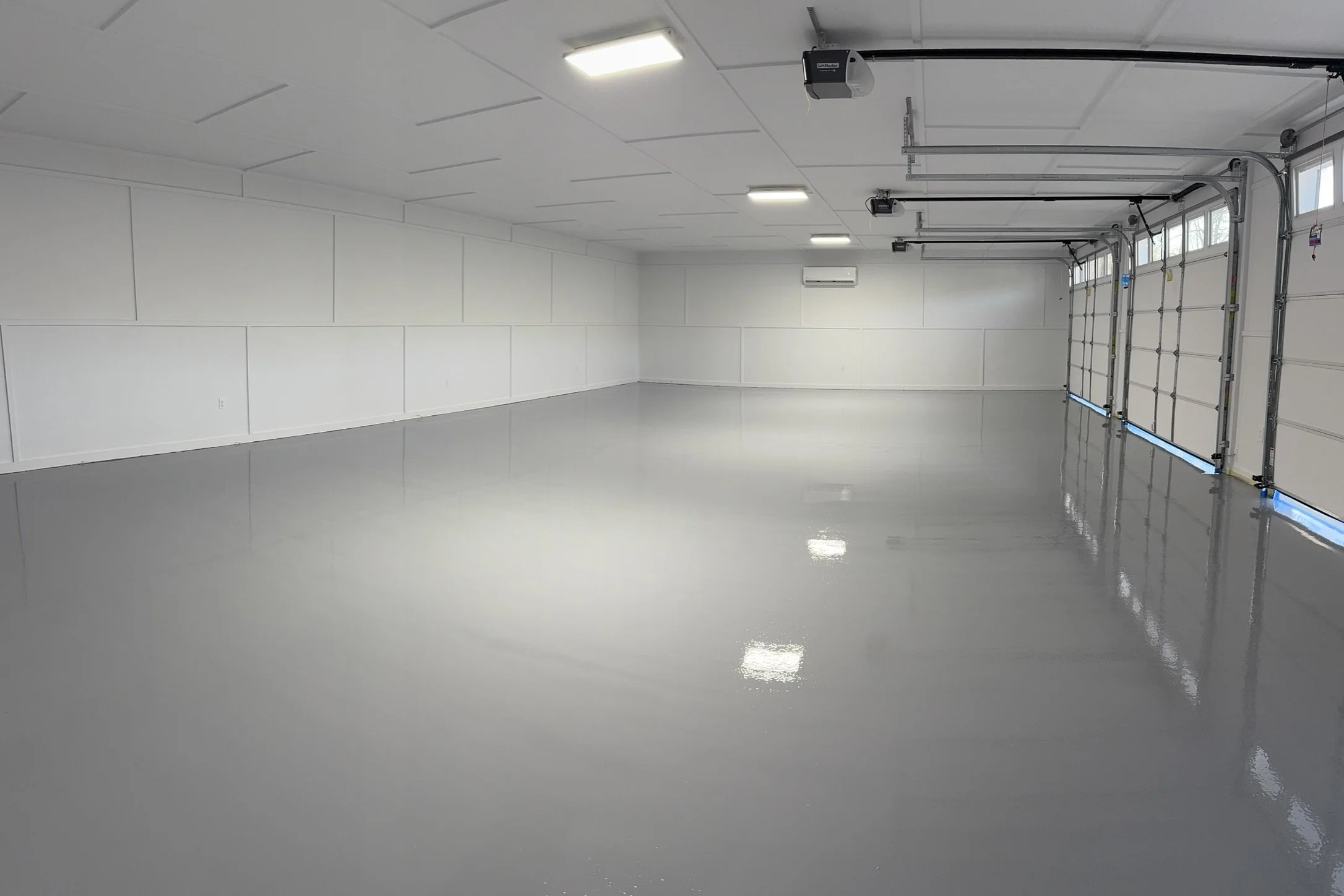 Empty clean garage with white walls, closed garage doors, and bright ceiling lights.