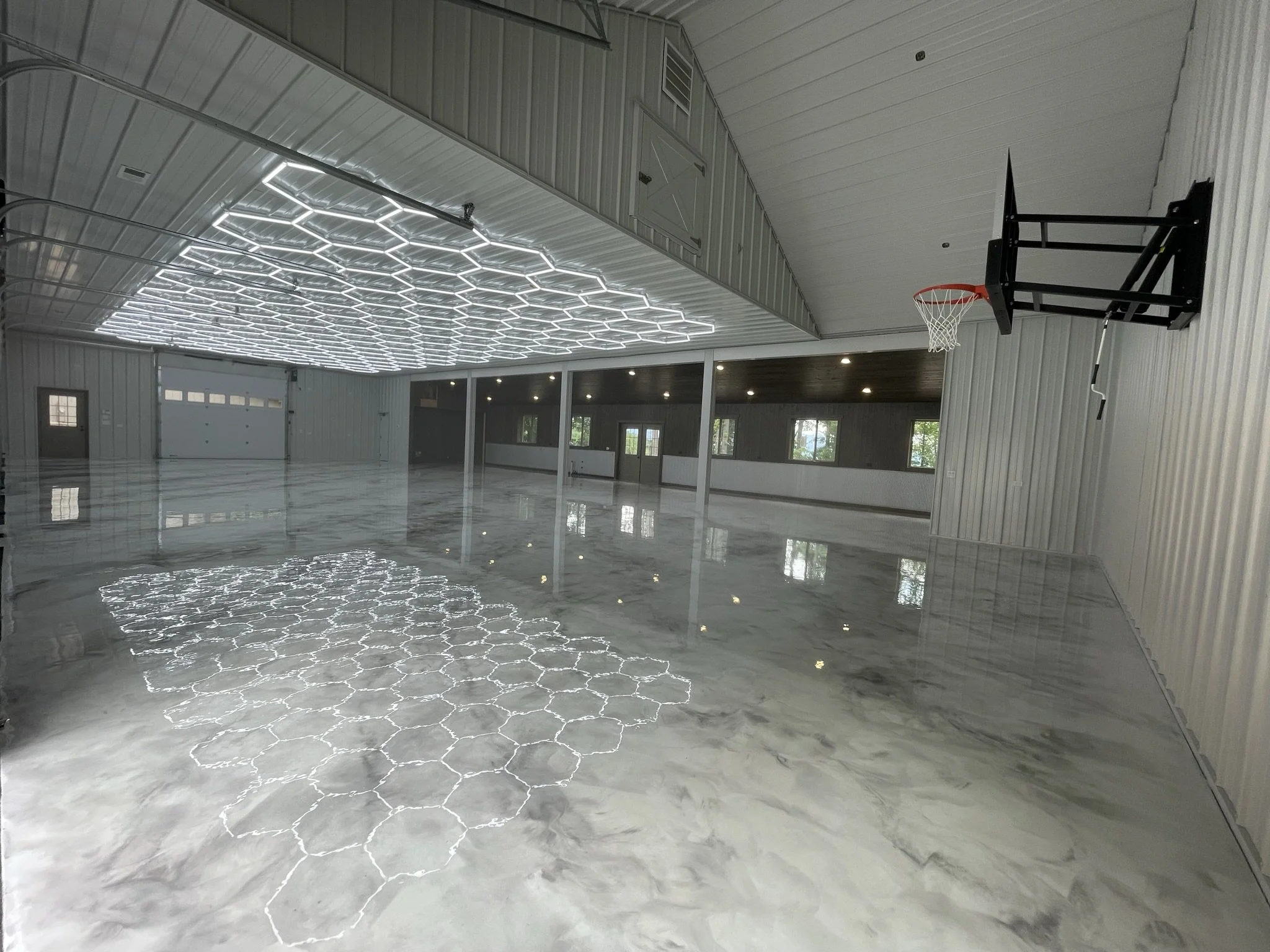 Empty indoor basketball court with a mounted hoop, polished marble floor, and a feature ceiling with hexagonal light fixtures.