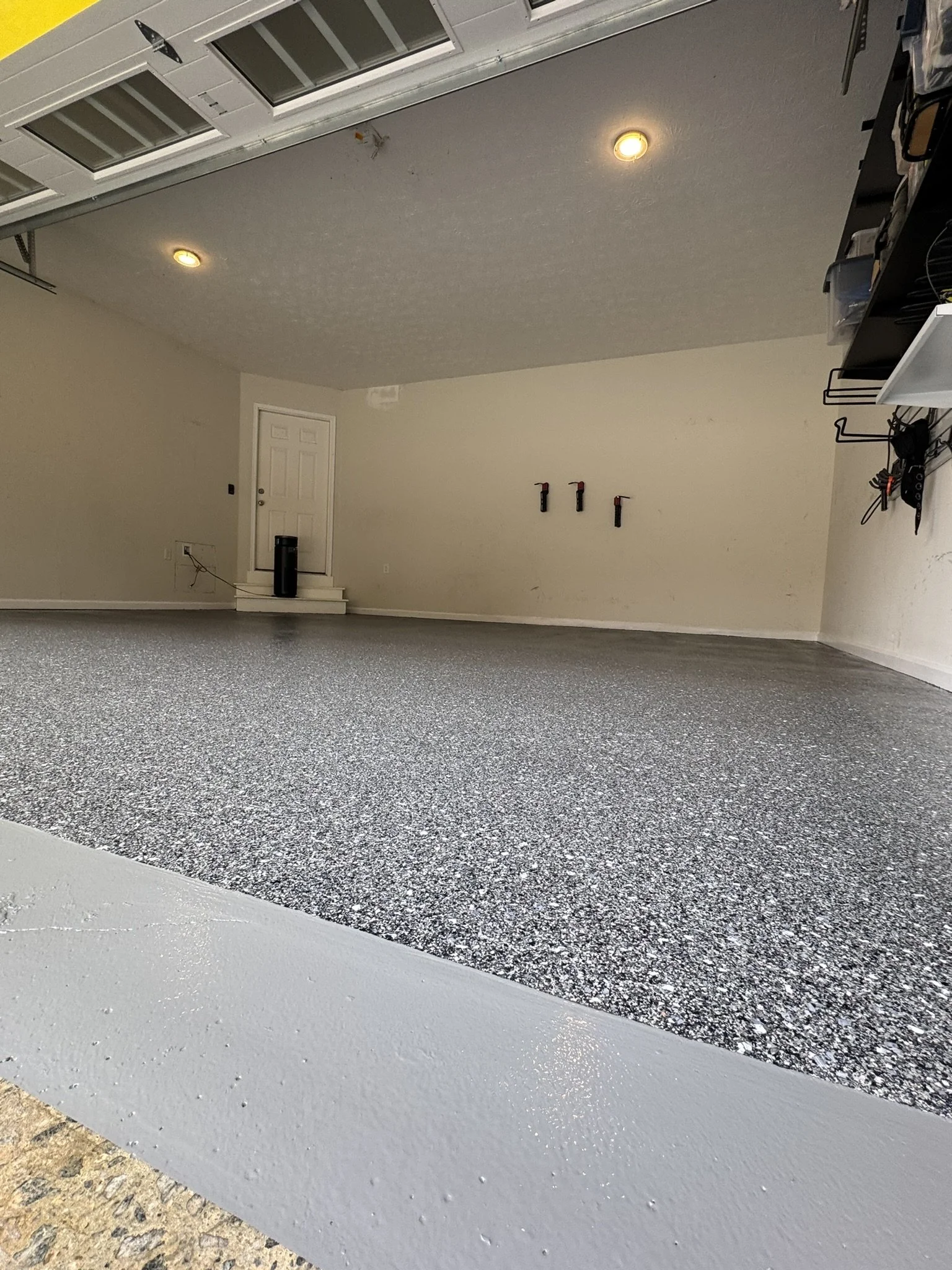 Empty garage with custom epoxy flake flooring and grey sealer on the apron of the garage