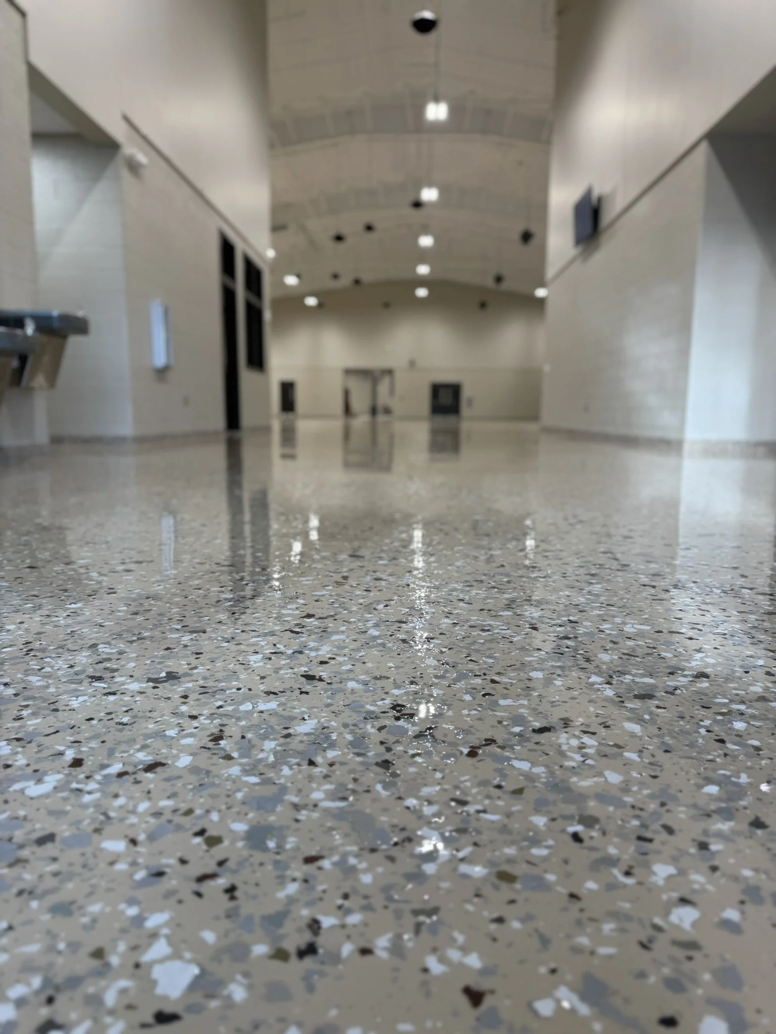 Empty indoor corridor with polished terrazzo flooring, beige walls, and a high arched ceiling with ceiling lights.