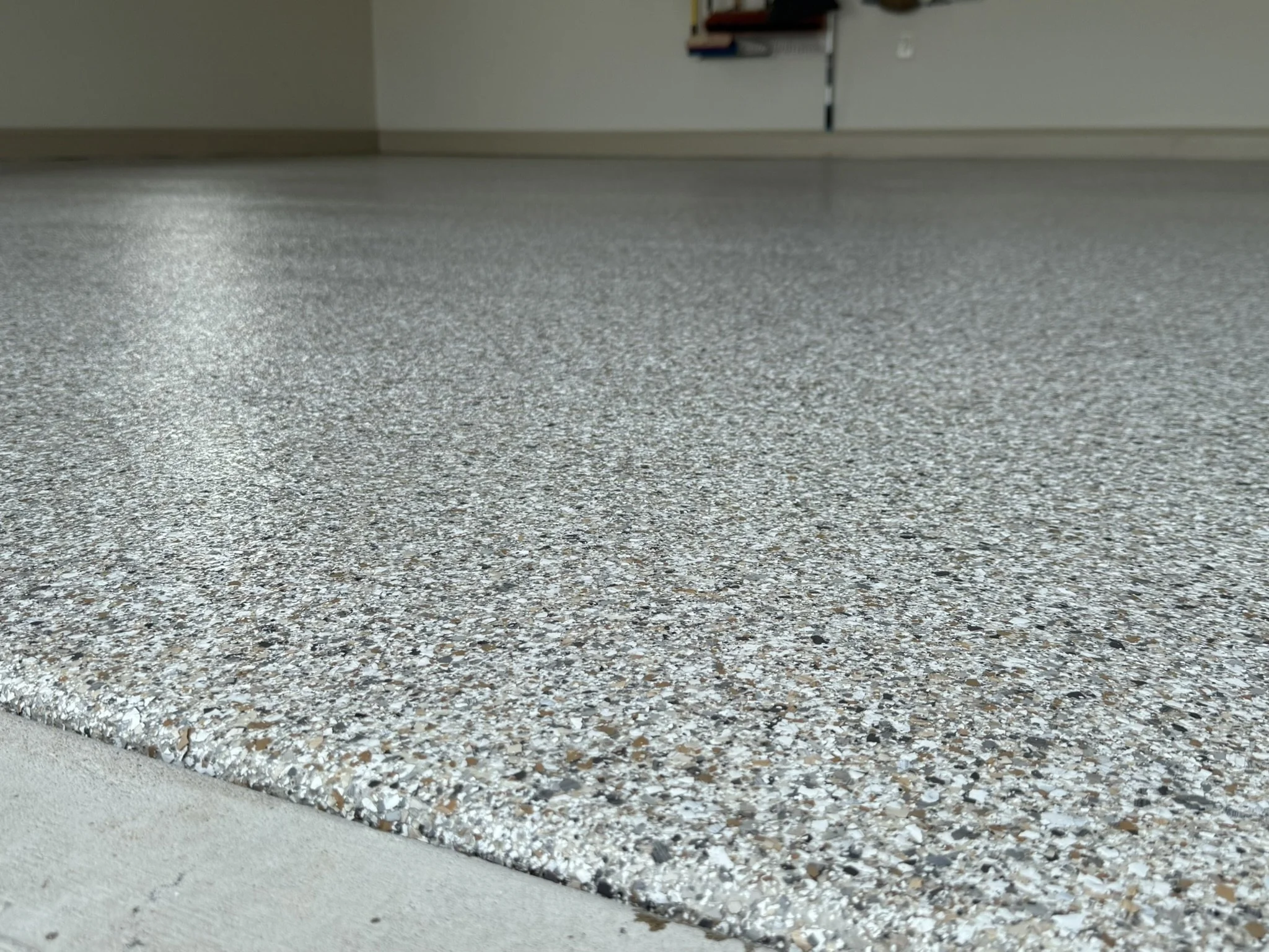 Close-up of a speckled, shiny epoxy resin floor in a room with a beige wall and a partially visible white cabinet.
