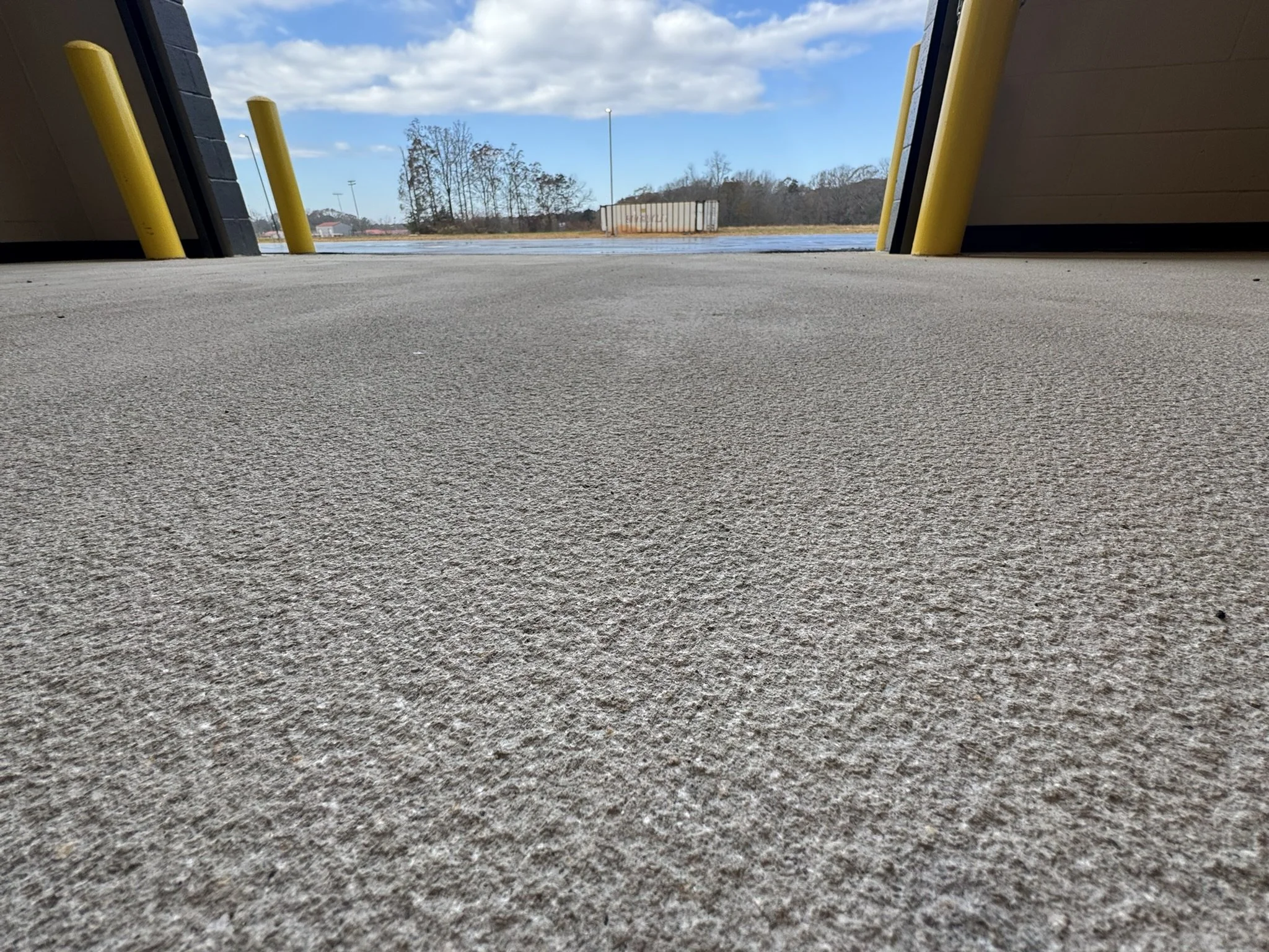 Low-angle shot of an empty parking lot with a concrete surface, yellow parking bumpers, and a partly cloudy sky in the background