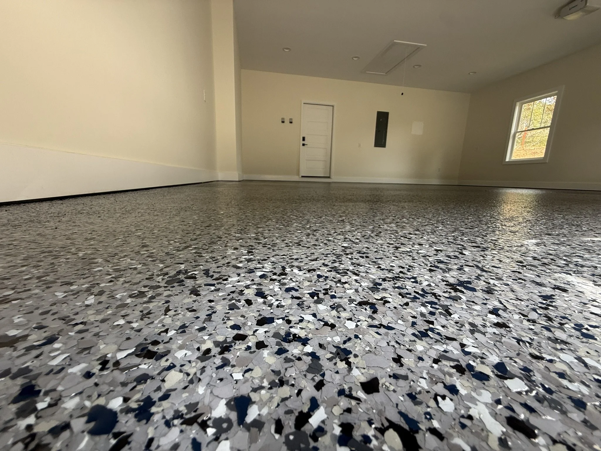 Empty room with terrazzo flooring, white walls, a white door, a window revealing trees outside, and ceiling fixtures.