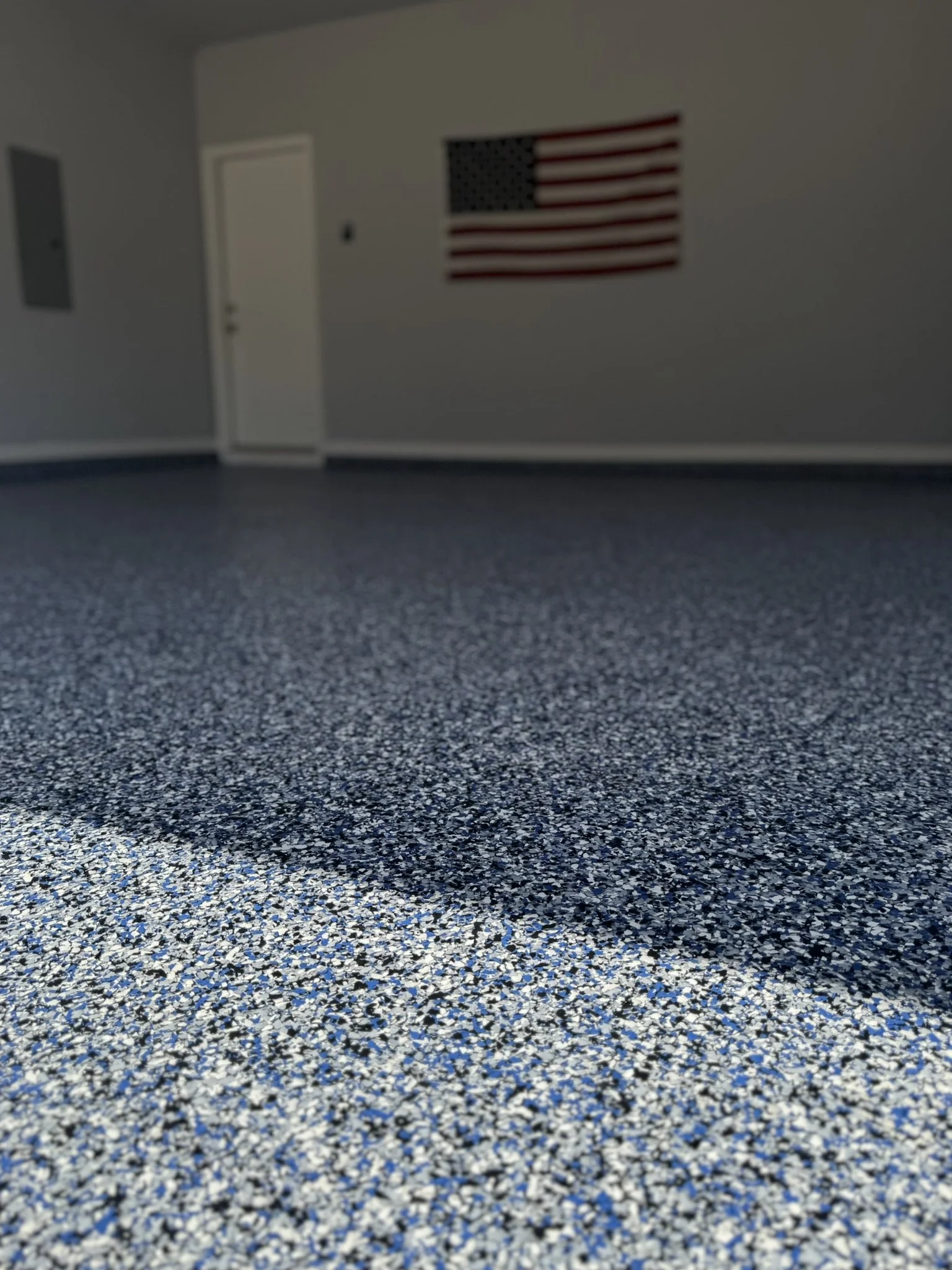 Empty room with an American flag on the wall, door, and blue speckled carpet floor.