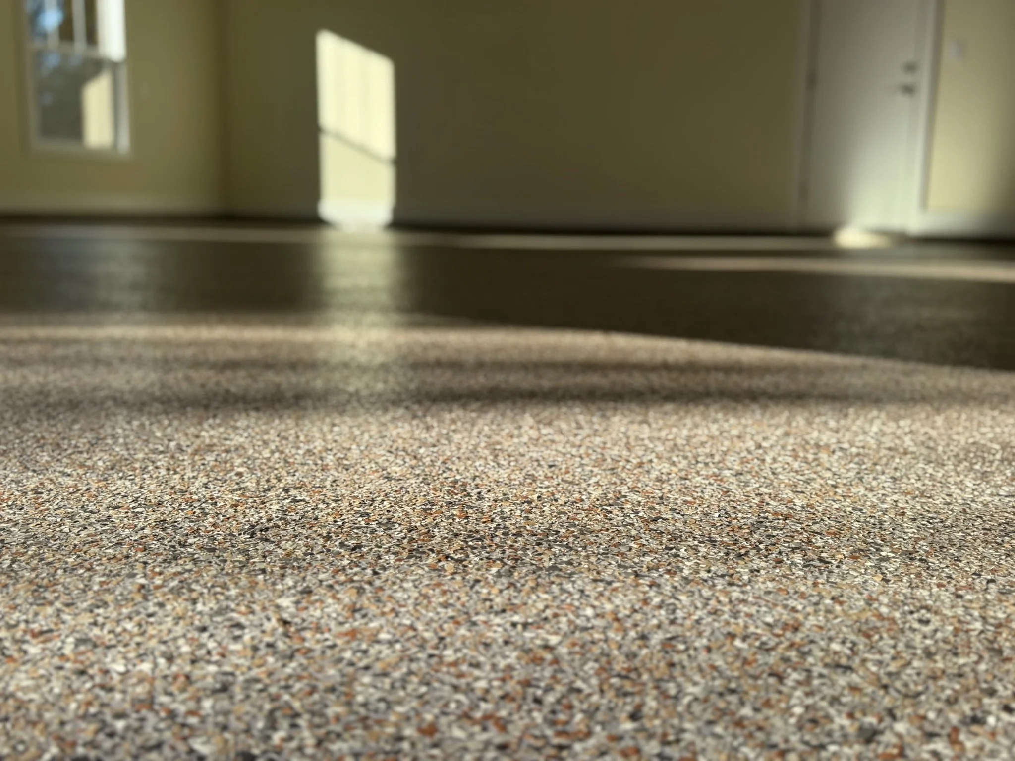 Close-up of a textured, multicolored carpeted floor leading to a door with sunlight casting shadows inside a room.