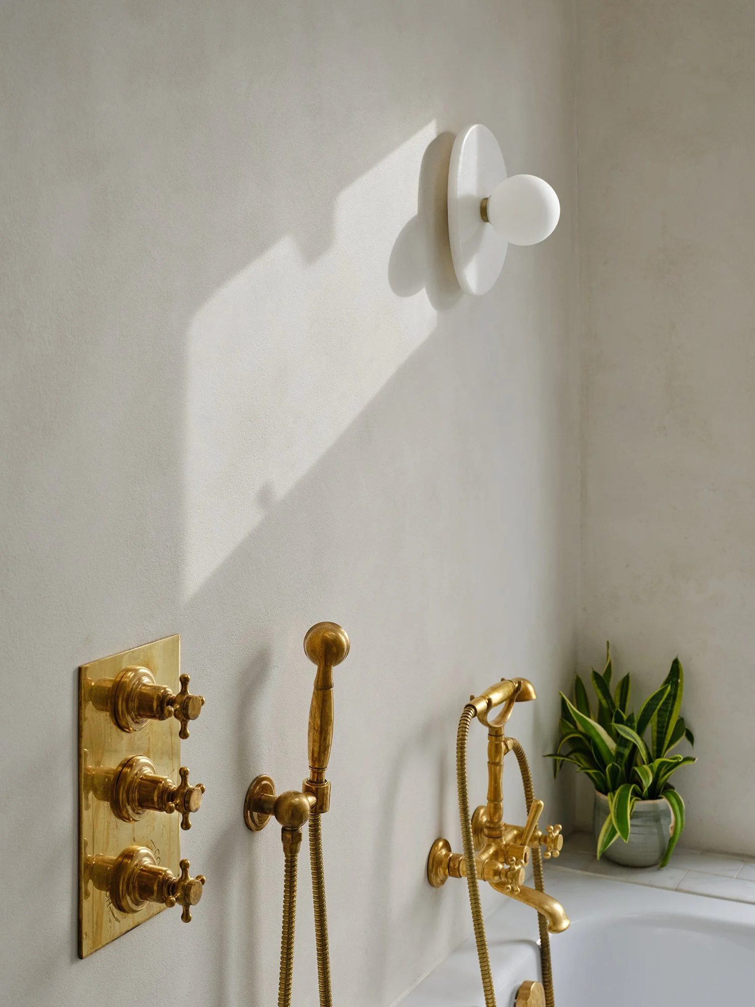 Microcement shower wall with a wall light, brass fittings and soft shadows, Cromwell Road, Teddington