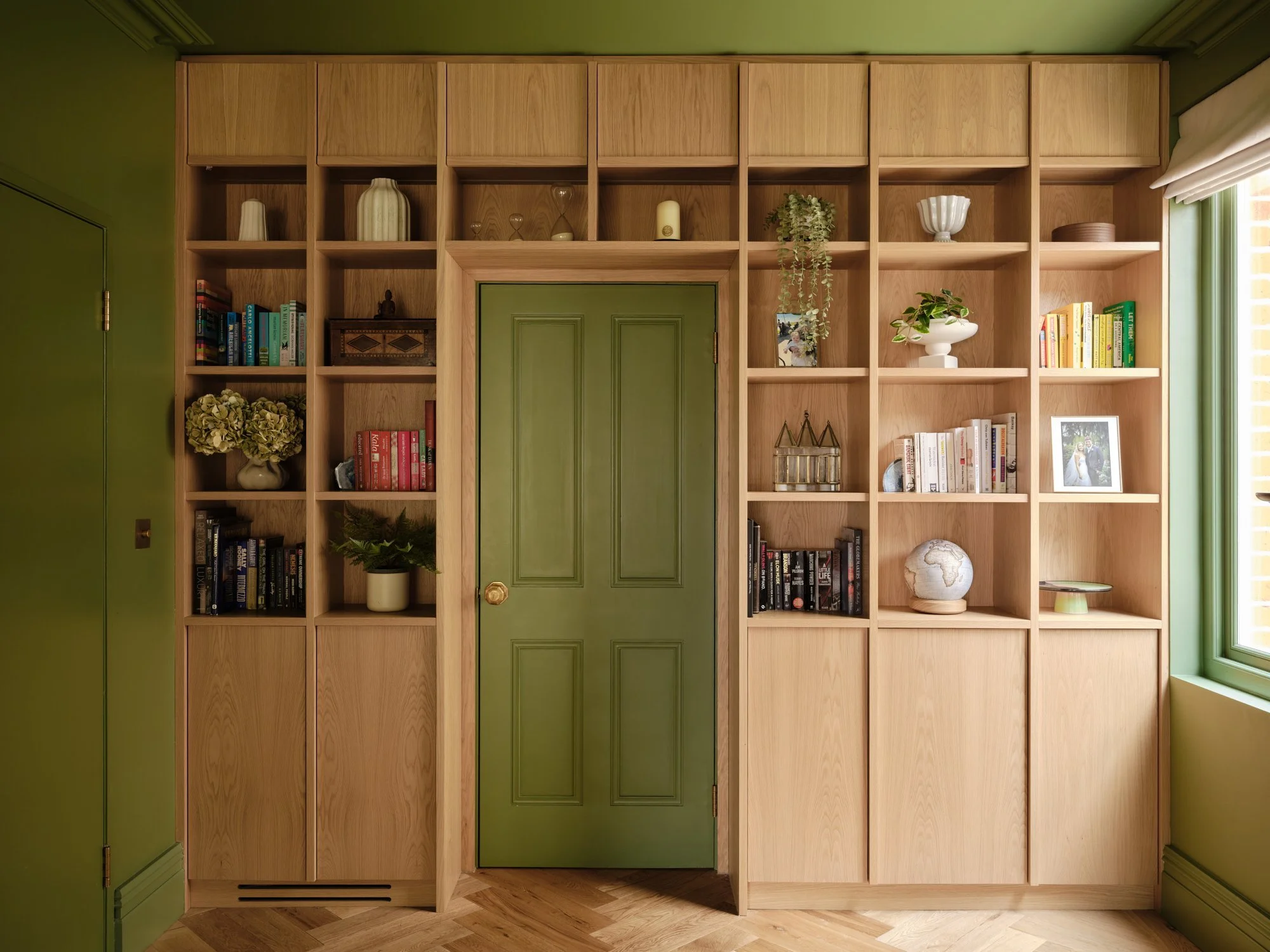 Oak bookshelves framing a green panelled door in the library, Cromwell Road, Teddington