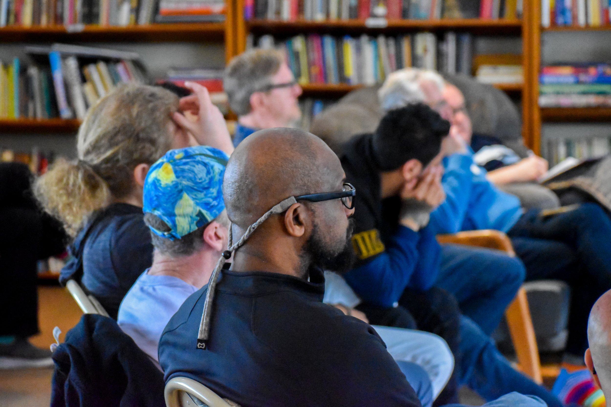 A group of people sitting and attentively listening in a room with bookshelves in the background.