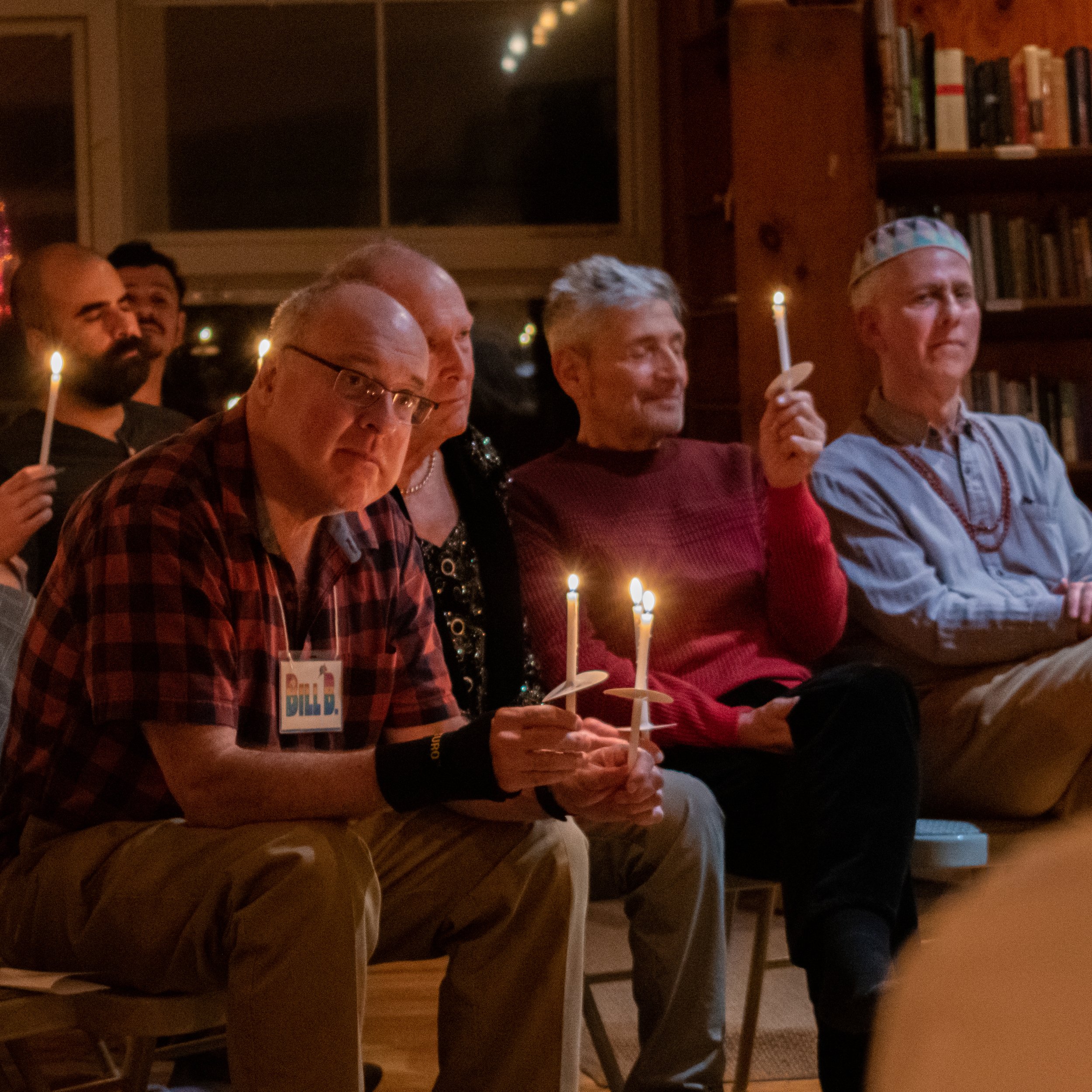 People sitting in a cozy room at night, some holding sparklers and candles, celebrating an event or gathering.