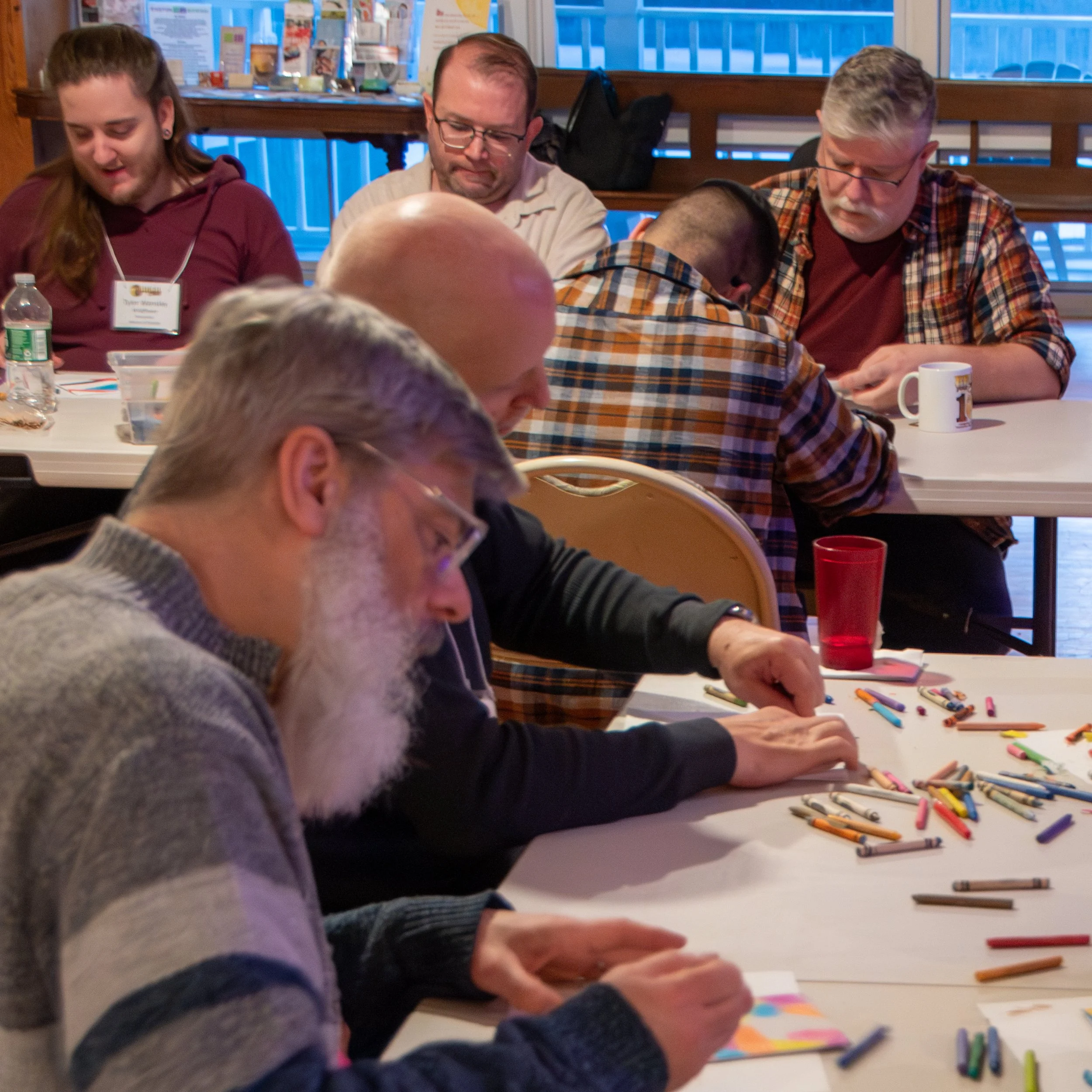 People sitting at a table engaging in a group activity or discussion, with art supplies such as colored chalks and sticky notes on the table.