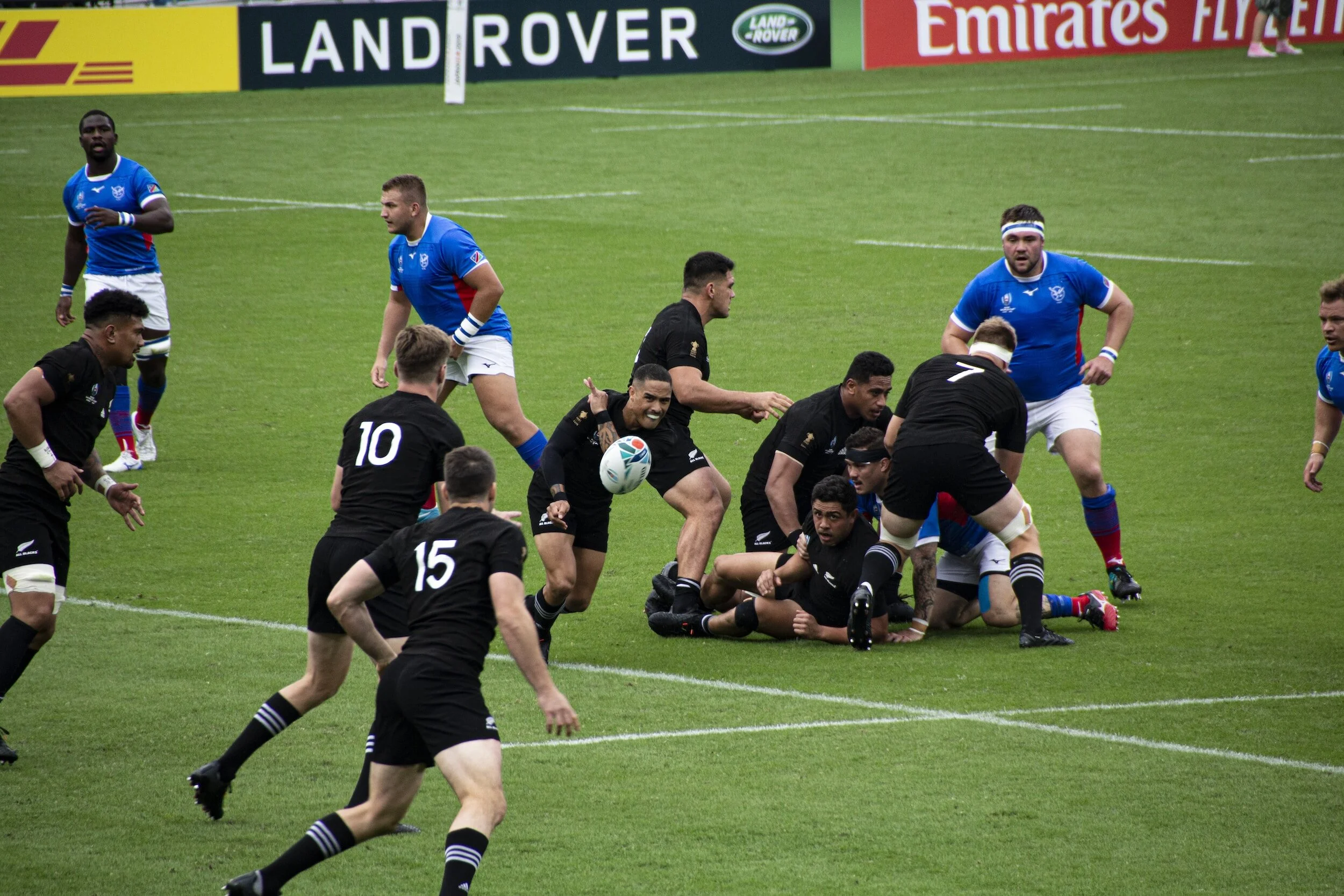 Rugby players in black and blue jerseys engaged in a tackle on a grassy field during a game.