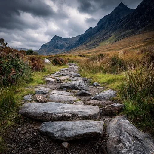A winding path with cloudy skies snaking up and around with craggy mountains on the right signifying the struggle of success.