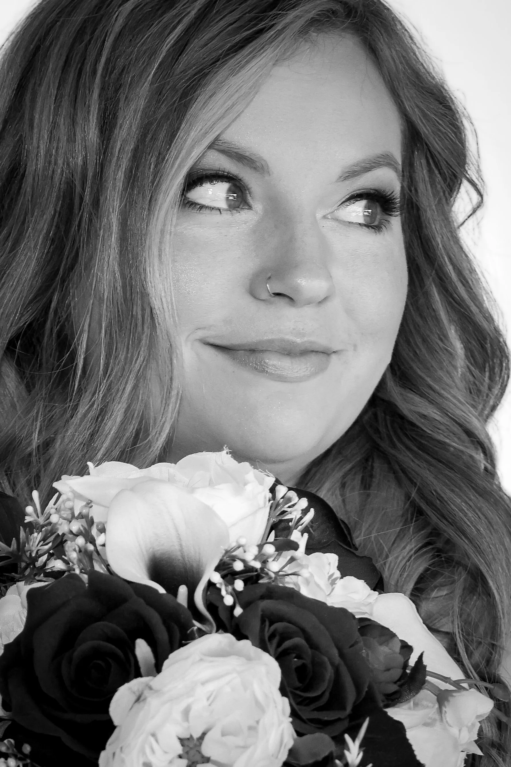 Black and white close-up photo of a woman with wavy hair holding a bouquet of flowers, smiling softly.