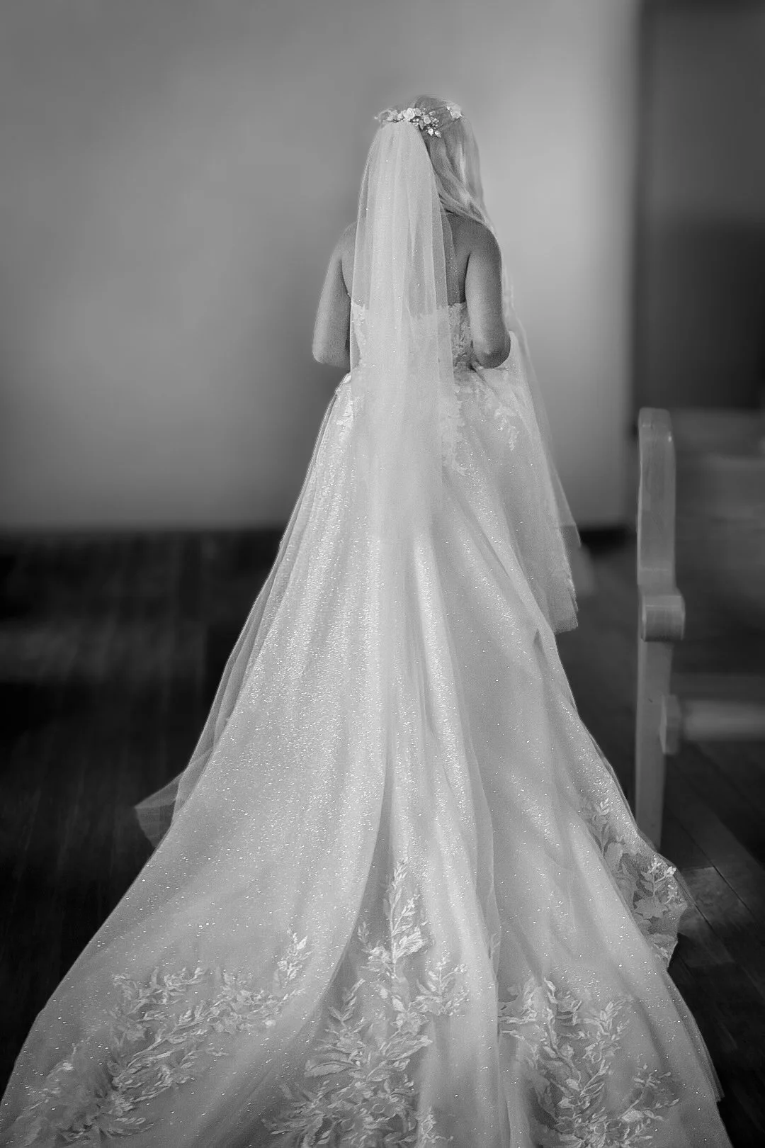Back view of a bride in a wedding dress with a long train and veil, standing indoors.