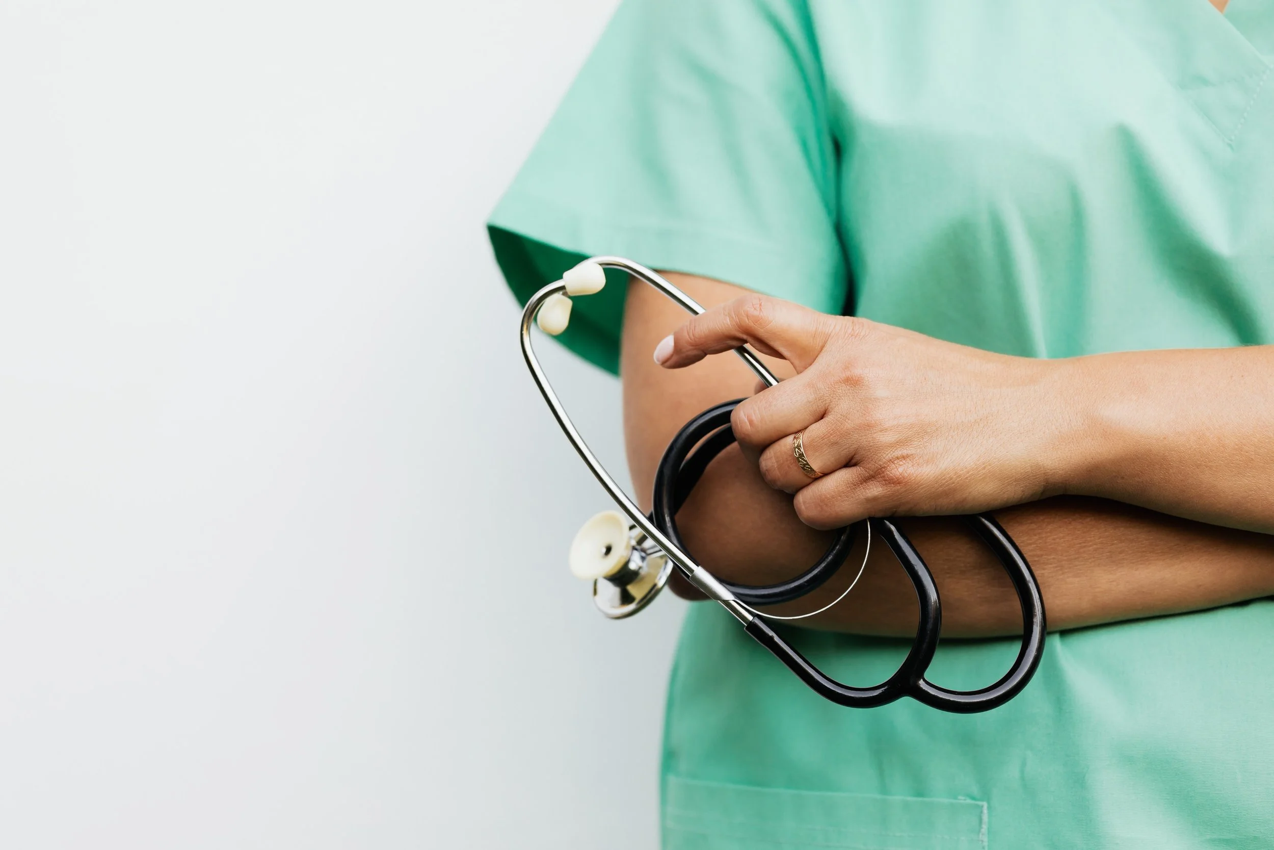 A person in a green medical scrub holds a stethoscope in their hand.