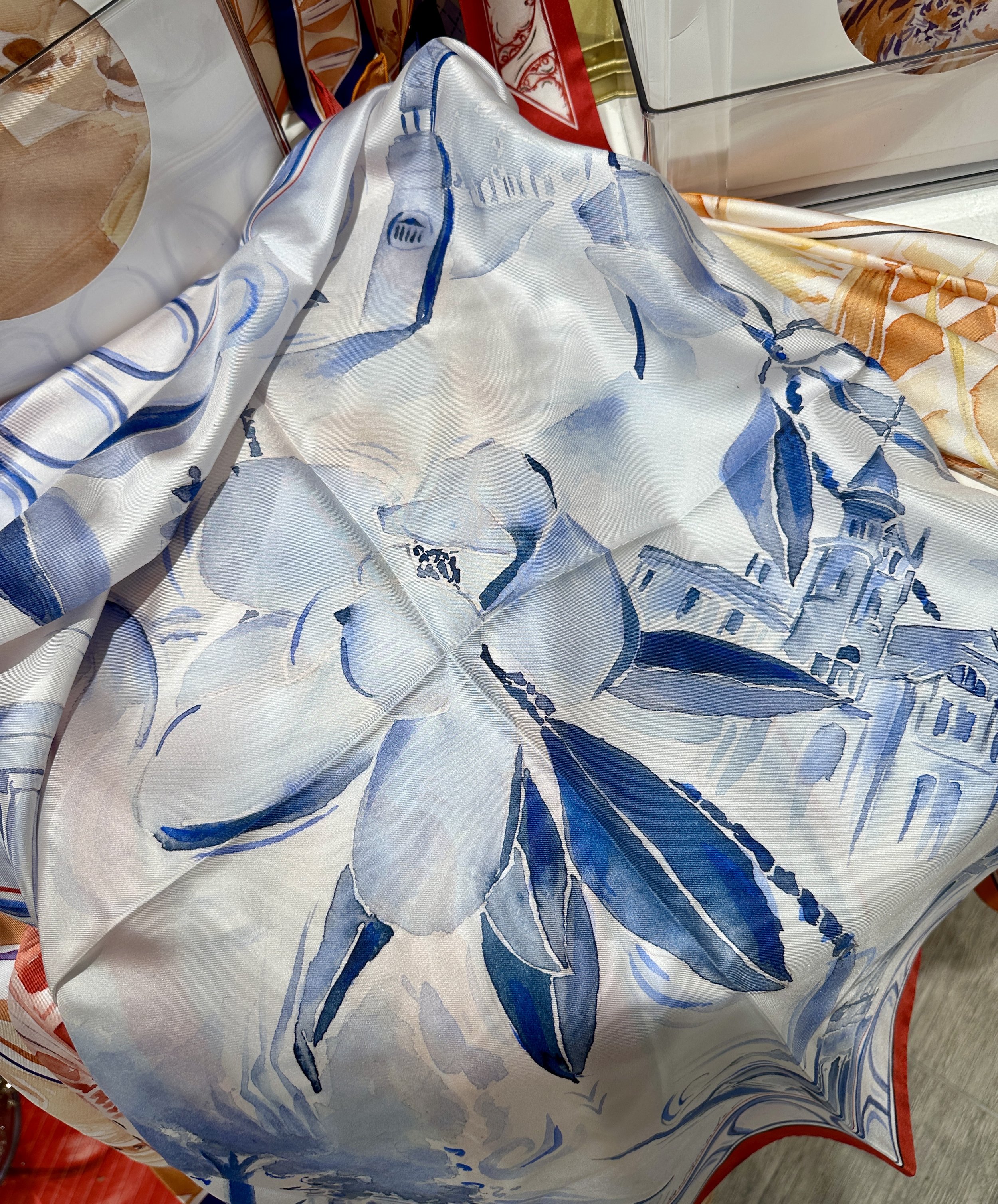 Ole Miss watercolor silk scarf by Megan Grinder, shown on the diamond, with magnolias and the Lyceum in blue inside a red border