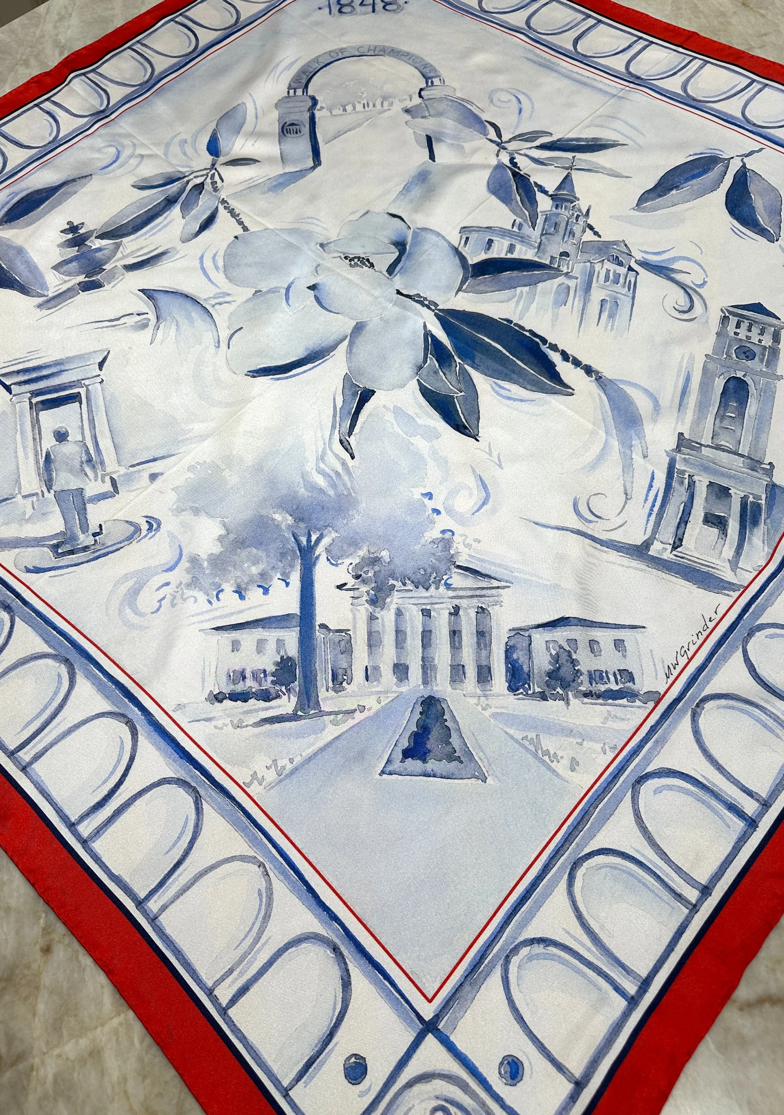 Ole Miss watercolor silk scarf by Megan Grinder, shown on the diamond, with magnolias and the Lyceum in blue inside a red border